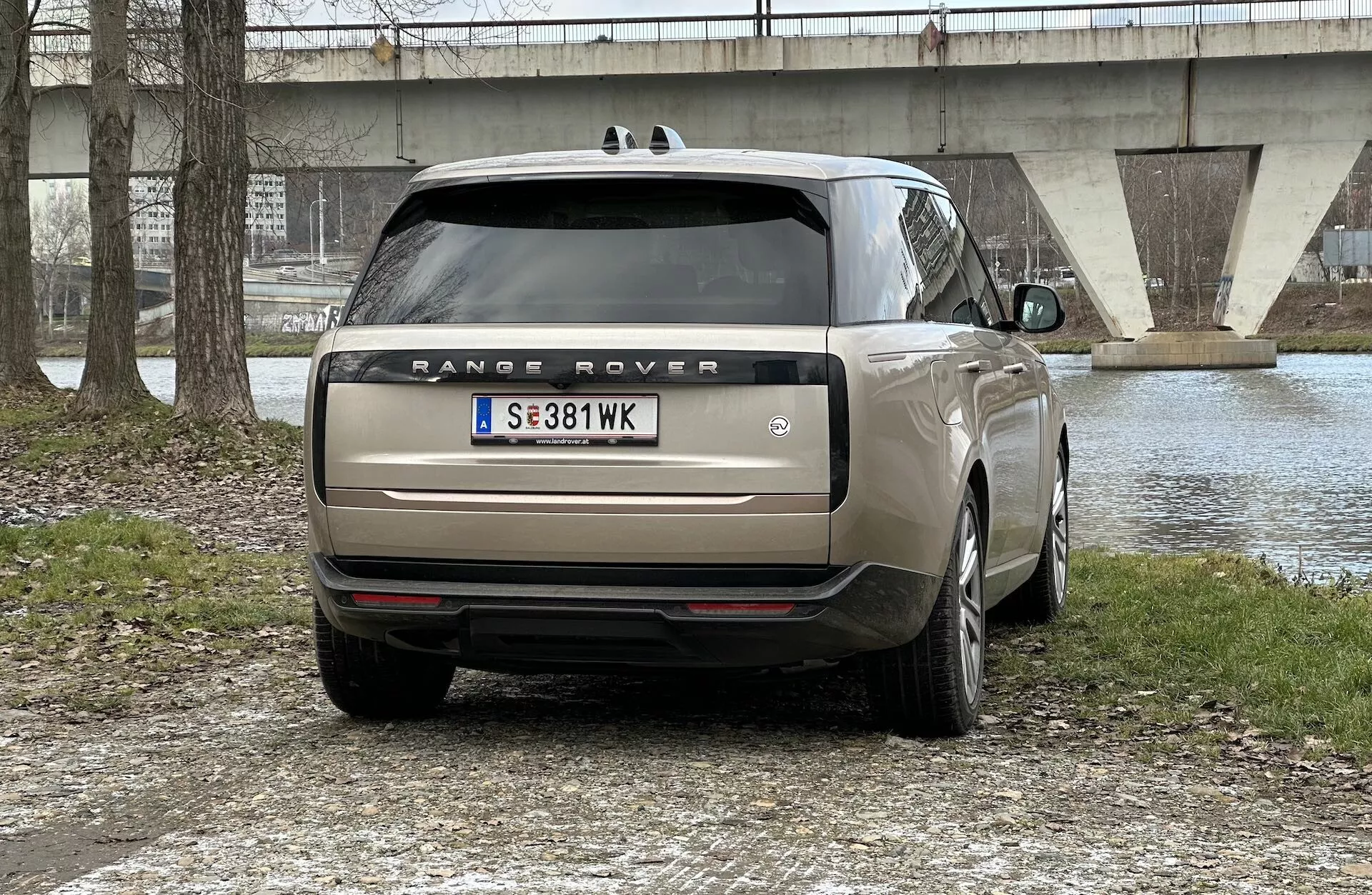 Vista traseira de um Range Rover 2021 estacionado ao ar livre com um corpo de água e uma ponte ao fundo, mostrando luzes traseiras LED, escape duplo, vidro fumê e rodas de liga leve multirraios.