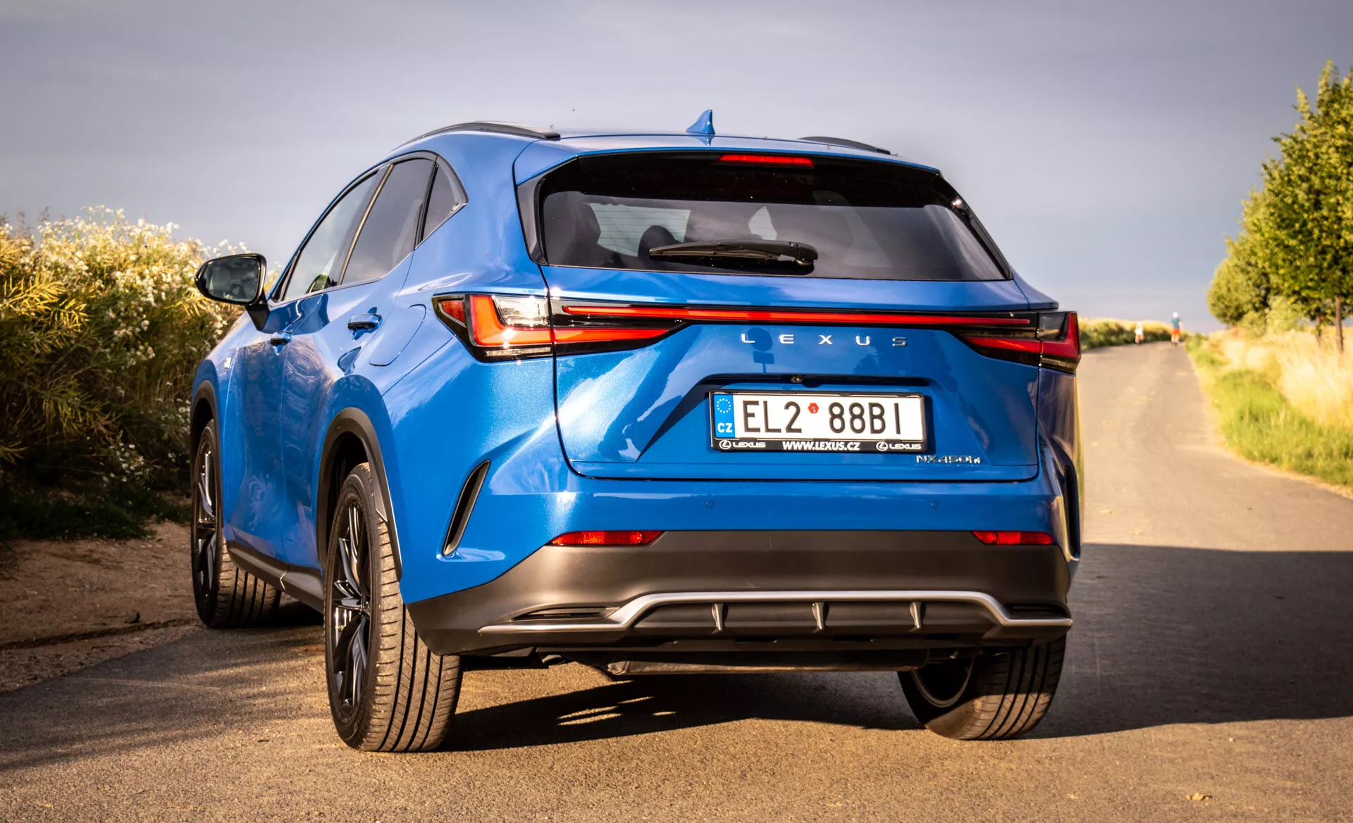 Vista traseira de um SUV crossover de luxo Lexus NX azul 2021 mostrando luzes traseiras LED, marcação Lexus, para-choque traseiro esportivo com difusor, tubos de escape duplos e outras características tecnológicas e de design de uma perspectiva de três quartos de baixo ângulo
