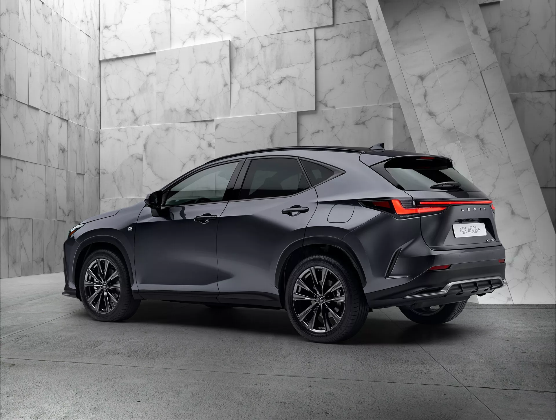 Vista traseira de três quartos de um SUV moderno Lexus NX 2021 em um ambiente de showroom. O lado direito e a traseira do veículo são claramente visíveis, destacando as luzes traseiras com design angular em LED, pintura escura e brilhante, rodas de vários raios e a linha do teto com possíveis trilhos de teto. O fundo neutro e texturizado contrasta bem com o design sofisticado do SUV.