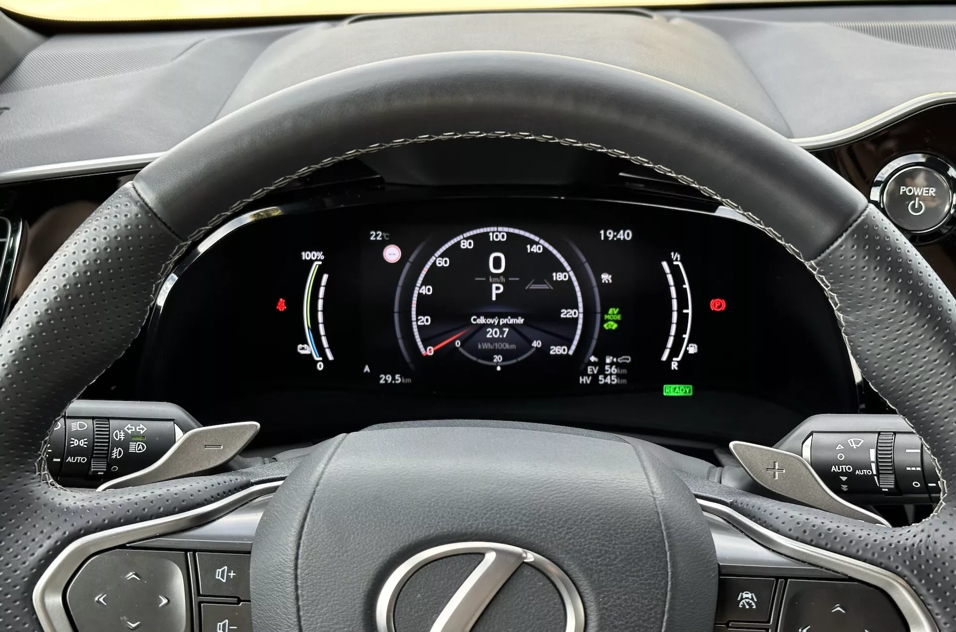 Vista do assento do condutor do volante e do painel de instrumentos digital do Lexus NX 2021, destacando indicadores da tecnologia híbrida, botões de controle de conforto e design interior ergonômico