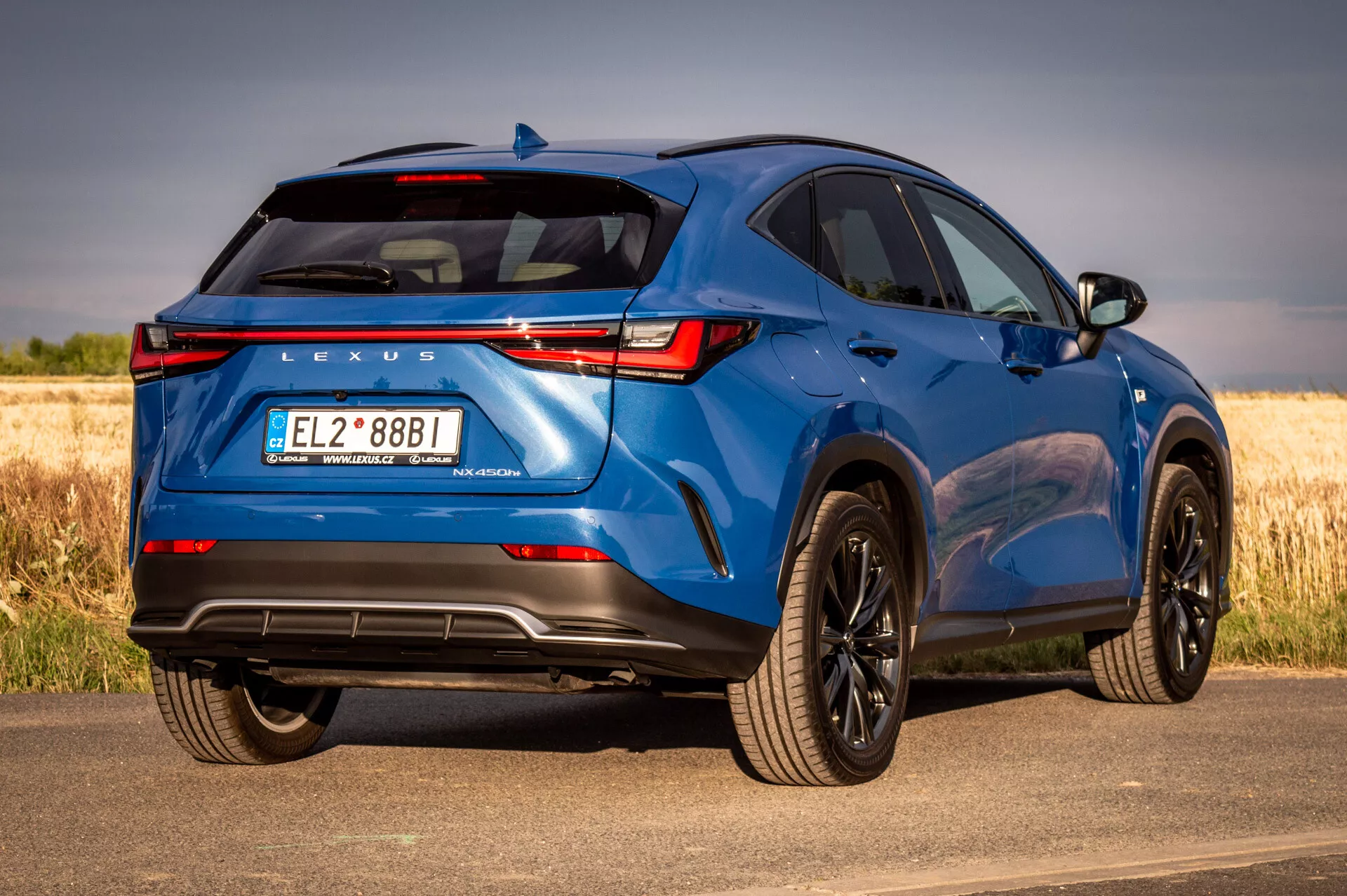 SUV Lexus NX azul 2021 em vista traseira de três quartos mostrando elementos de design e recursos tecnológicos em um dia ensolarado com fundo natural