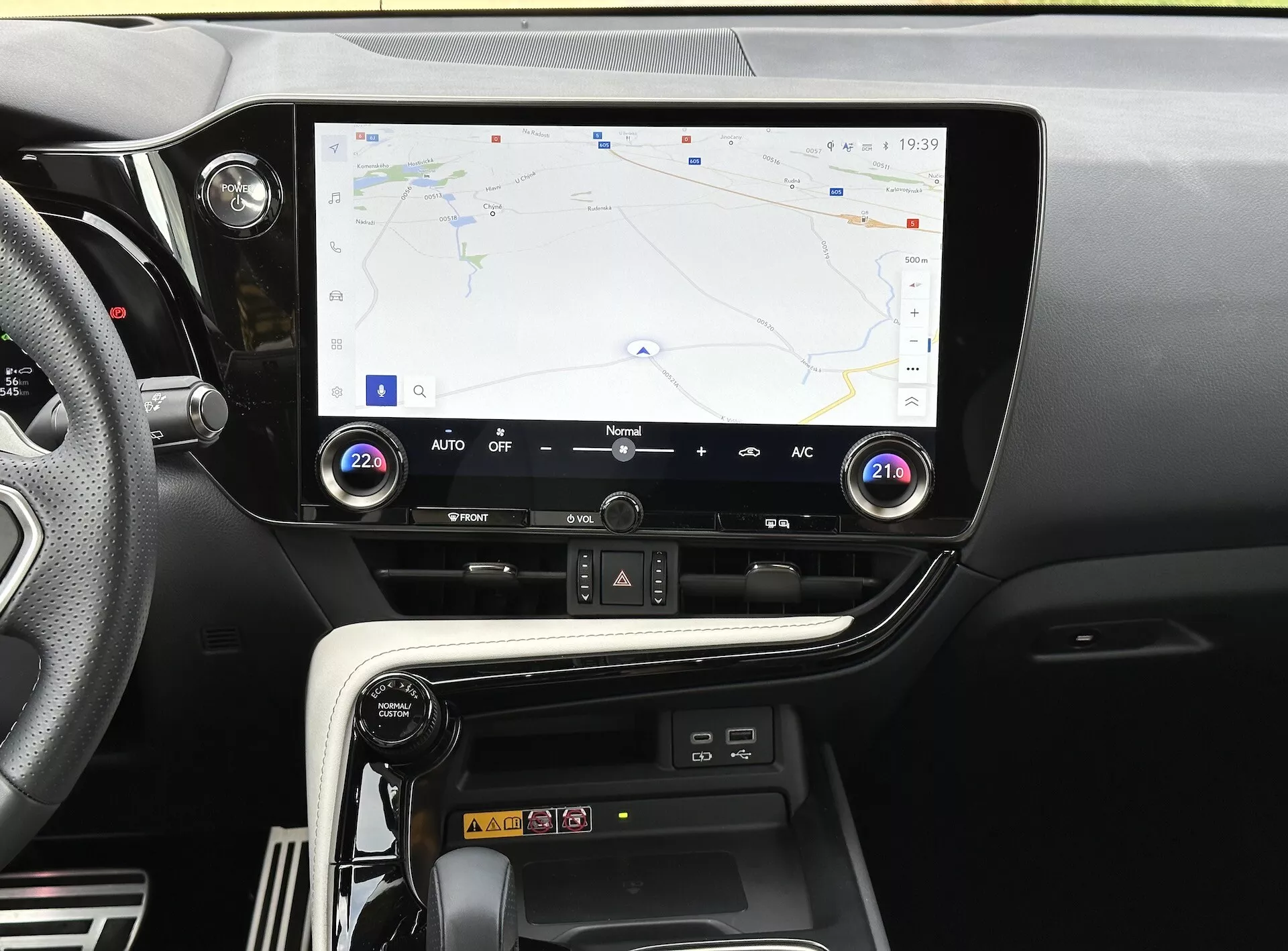 Console central do Lexus NX 2021 com tela sensível ao toque exibindo navegação GPS, botões e comandos para controle climático, e compartimento para carregamento de smartphone