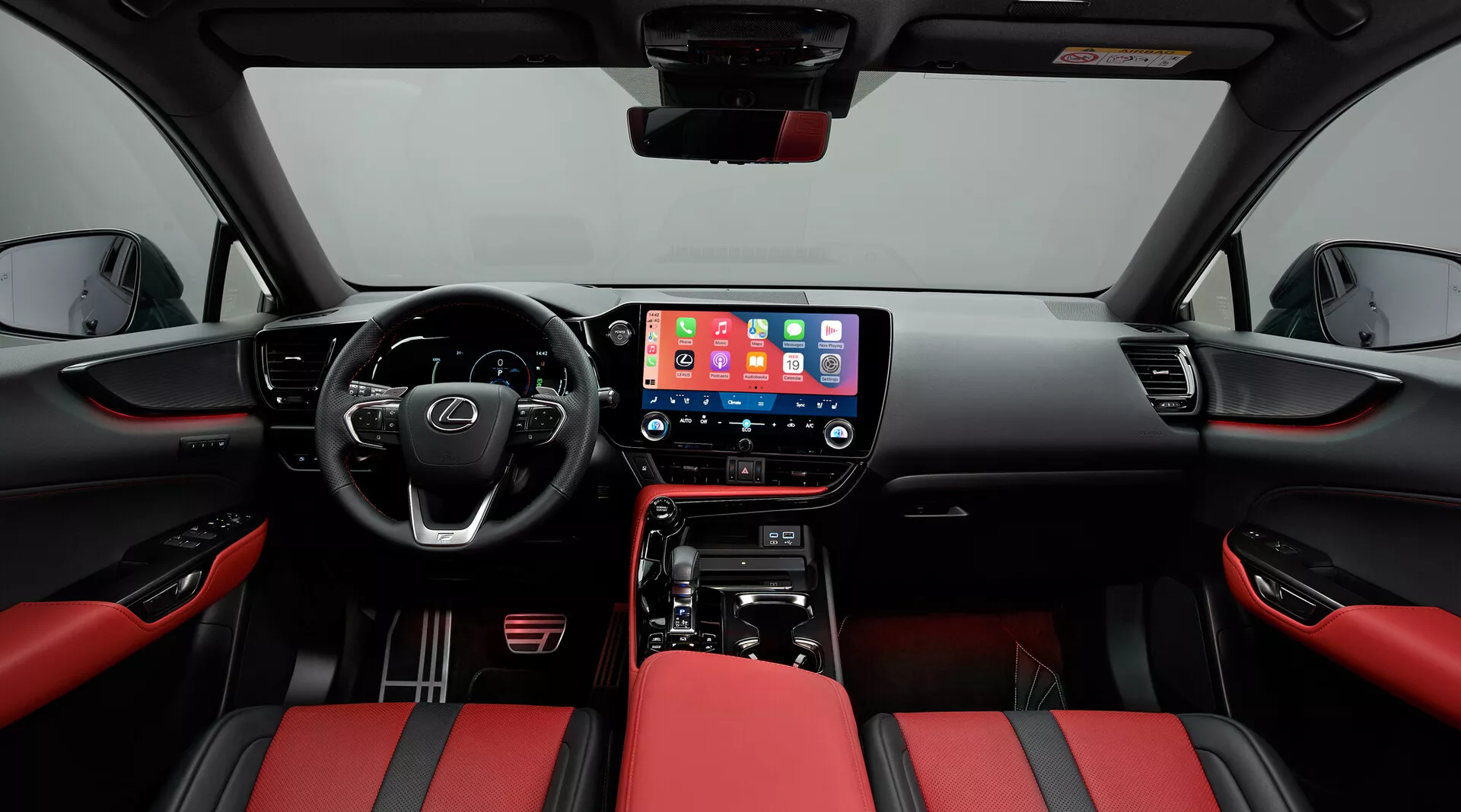Interior do Lexus NX 2021 focado na cabine dianteira, tirado de uma posição central. A perspectiva de grande ângulo mostra o painel com uma grande tela central de infotainment exibindo uma interface móvel, controles físicos do ar condicionado e uma alavanca de câmbio para transmissão automática. O volante multifuncional com botões de controle sugere recursos avançados. Os assentos são estofados em couro vermelho e preto em dois tons, proporcionando um visual esportivo. Os painéis das portas combinam com o tema vermelho e preto com controles de vidros elétricos e uma grade de alto-falante visível, enfatizando modernidade e luxo.