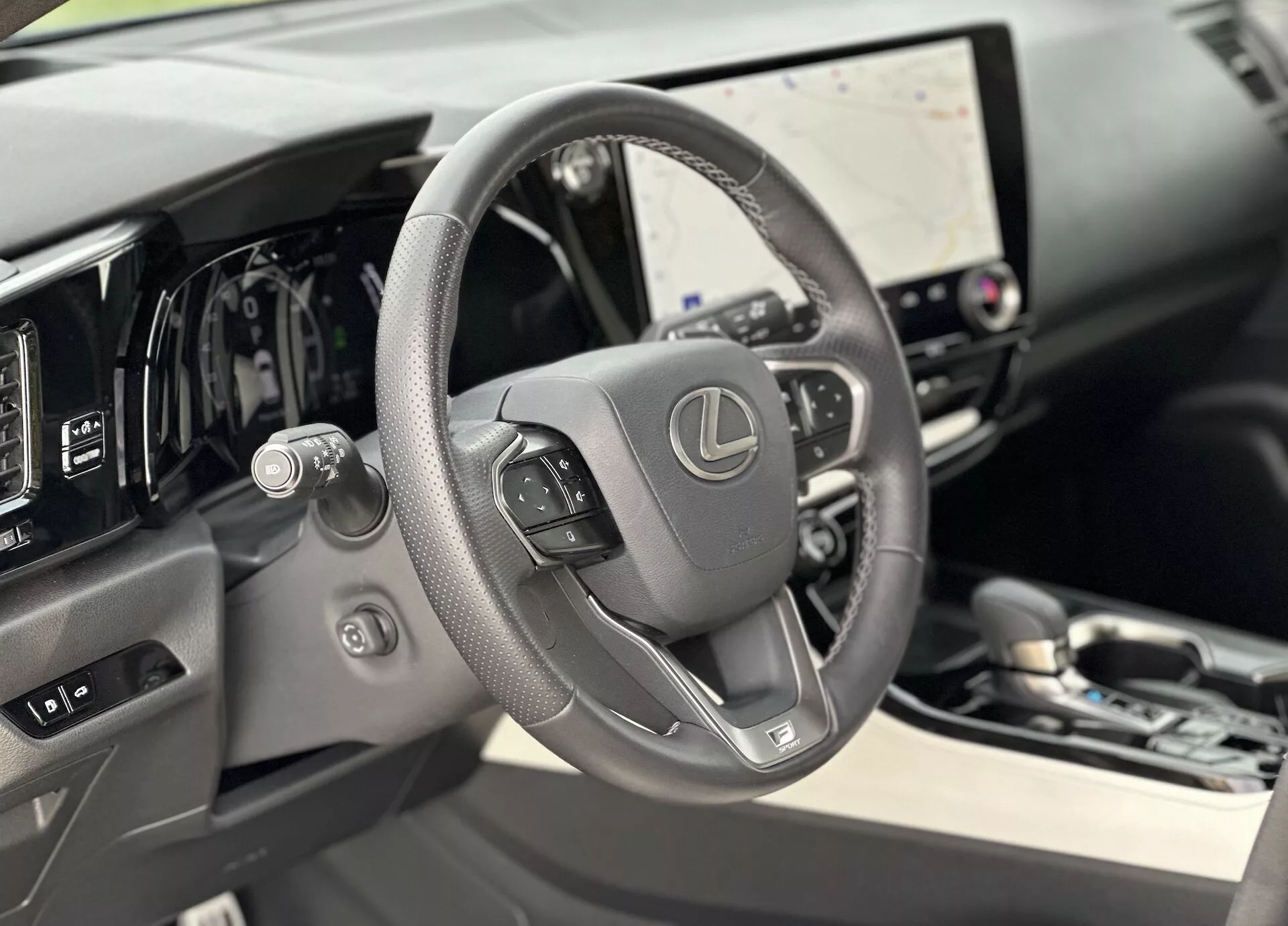 Vista interior do Lexus NX 2021 focada no volante revestido a couro com controles montados e painel digital atrás, apresentando grande tela touchscreen de infotainment e dicas sutis de luxo nos materiais de alta qualidade