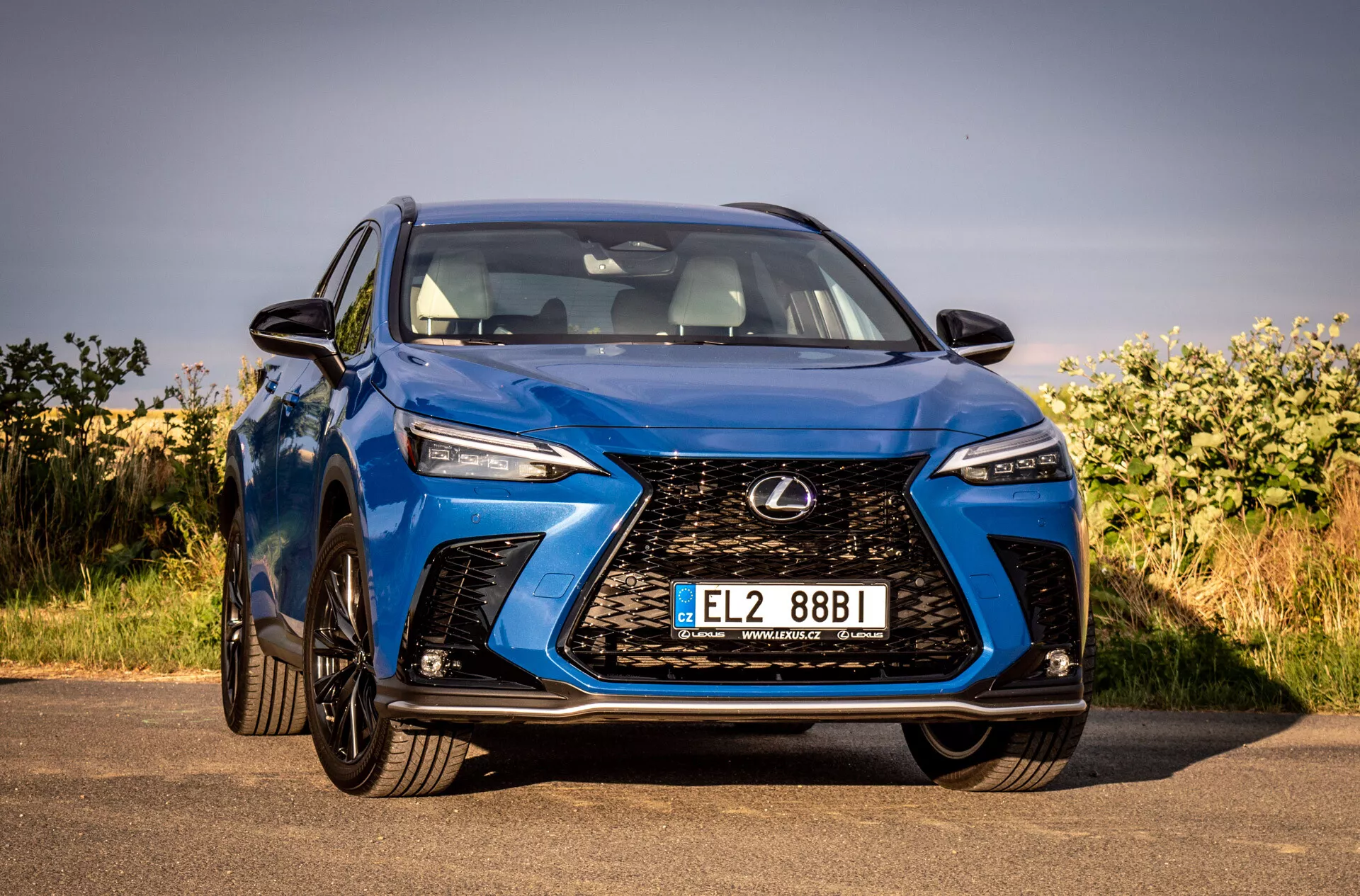 Vista frontal de um SUV Lexus NX 2021 azul destacando sua grade do tipo spindle intricada, faróis LED angulares, acabamento brilhante e design aerodinâmico, estacionado ao ar livre sob céus limpos