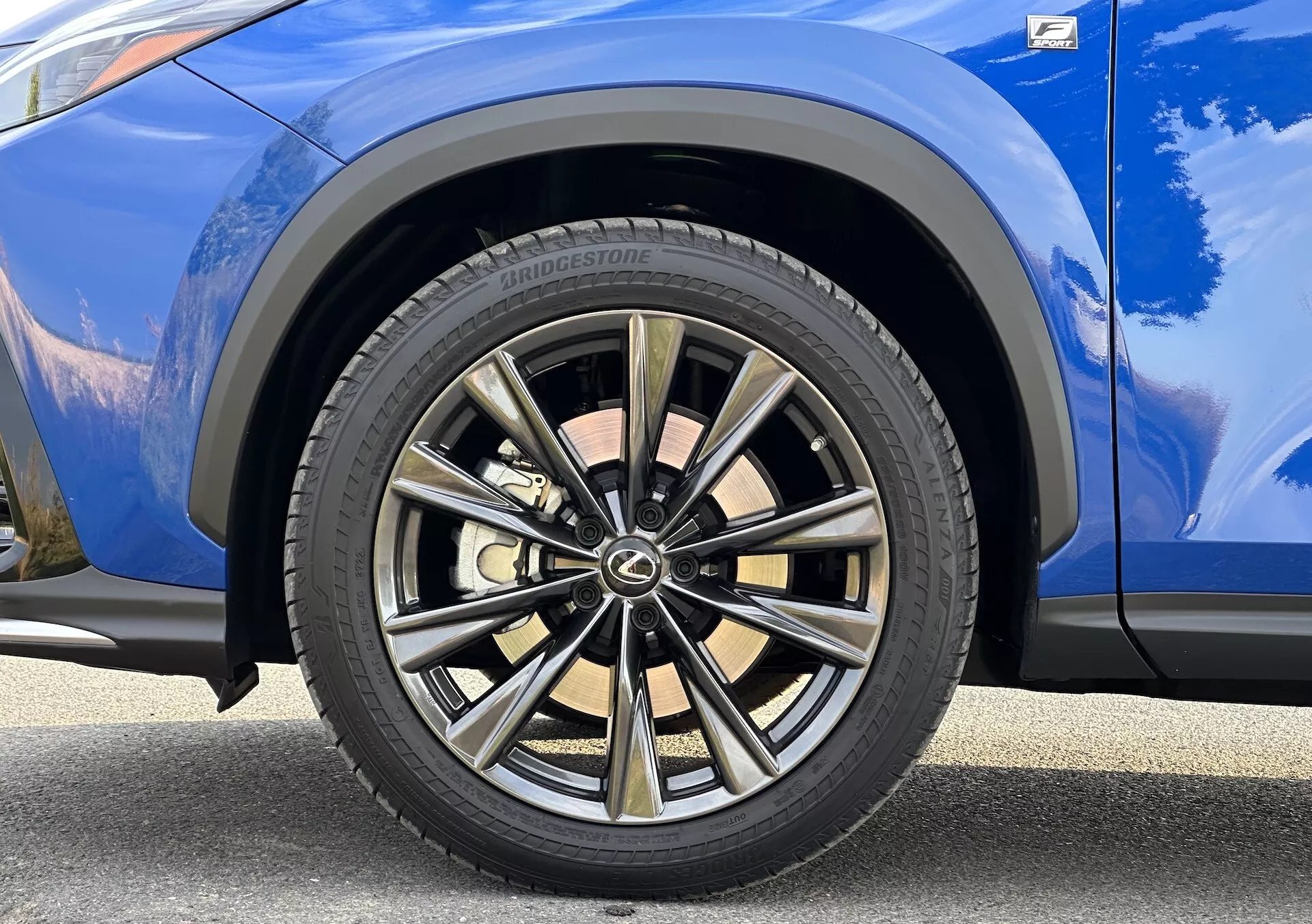 Vista detalhada do pneu dianteiro do lado do passageiro da Lexus NX 2021 com design de multi-raios com acabamento em duas tonalidades e pneu Bridgestone, com carroceria azul vibrante