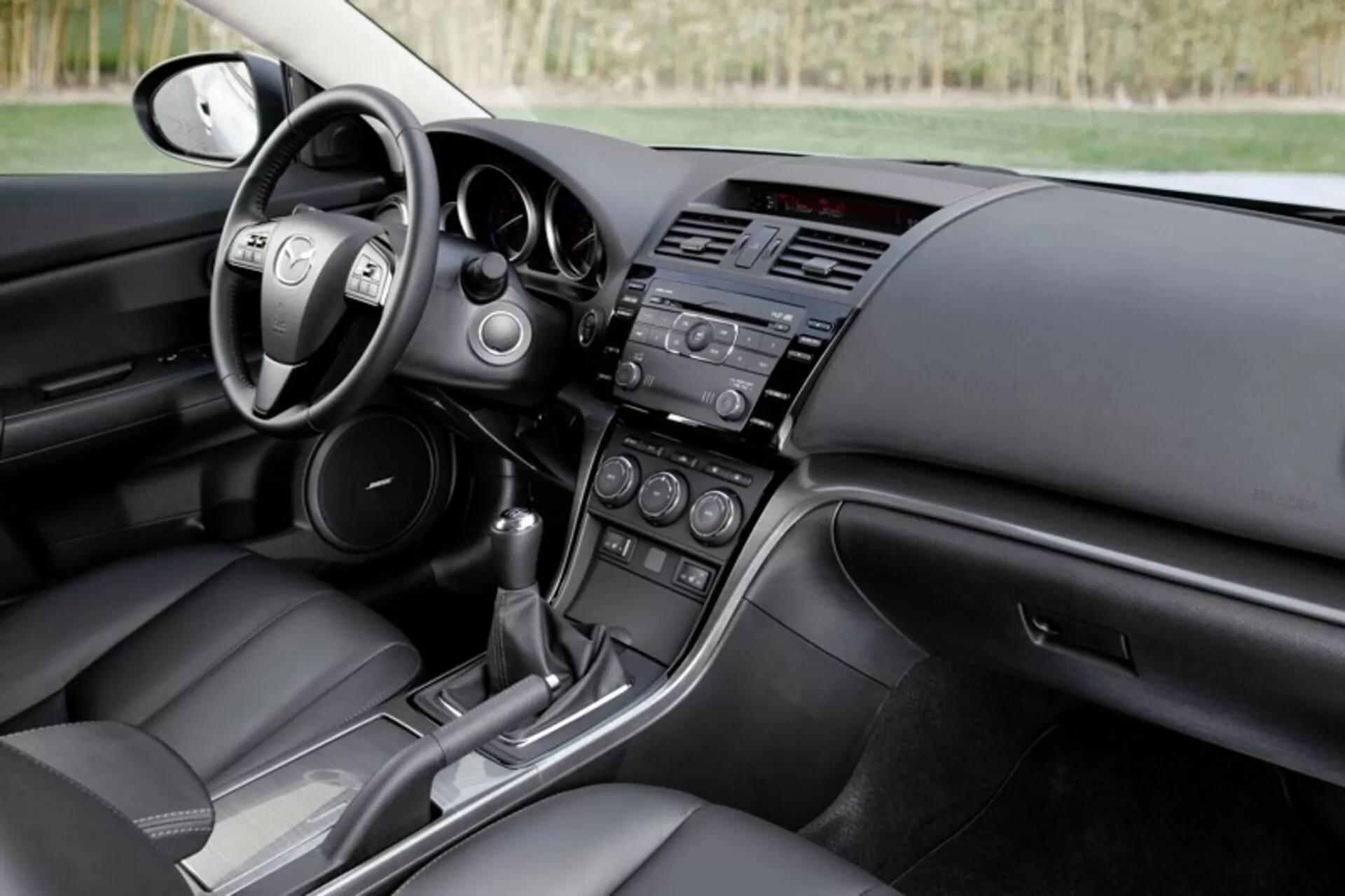 Interior do sedan Mazda 6 de 2008 mostrando o cockpit do motorista e a vista do painel do passageiro com controles no volante, sistemas de infotainment e controle climático, e consola de transmissão automática, realçando o design moderno e as características tecnológicas do carro.