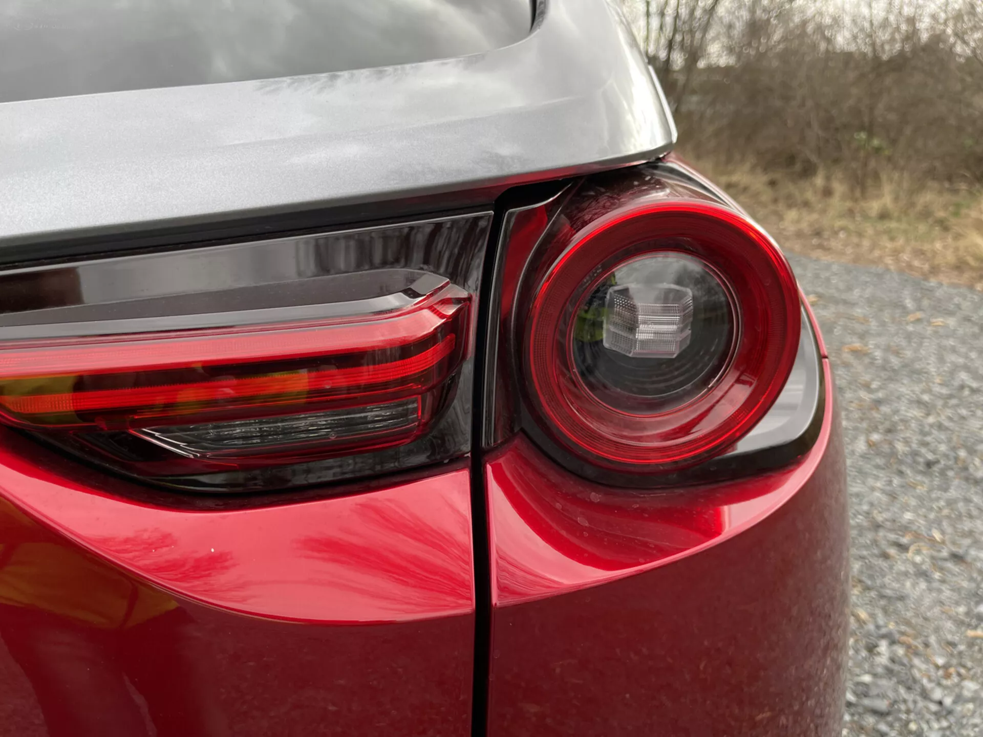 Vista detalhada do canto traseiro de um Mazda MX-30 2020 mostrando o design detalhado da luz traseira, pintura vermelha brilhante e reflexo no seu corpo, destacando a tecnologia de iluminação de veículos modernos e design.