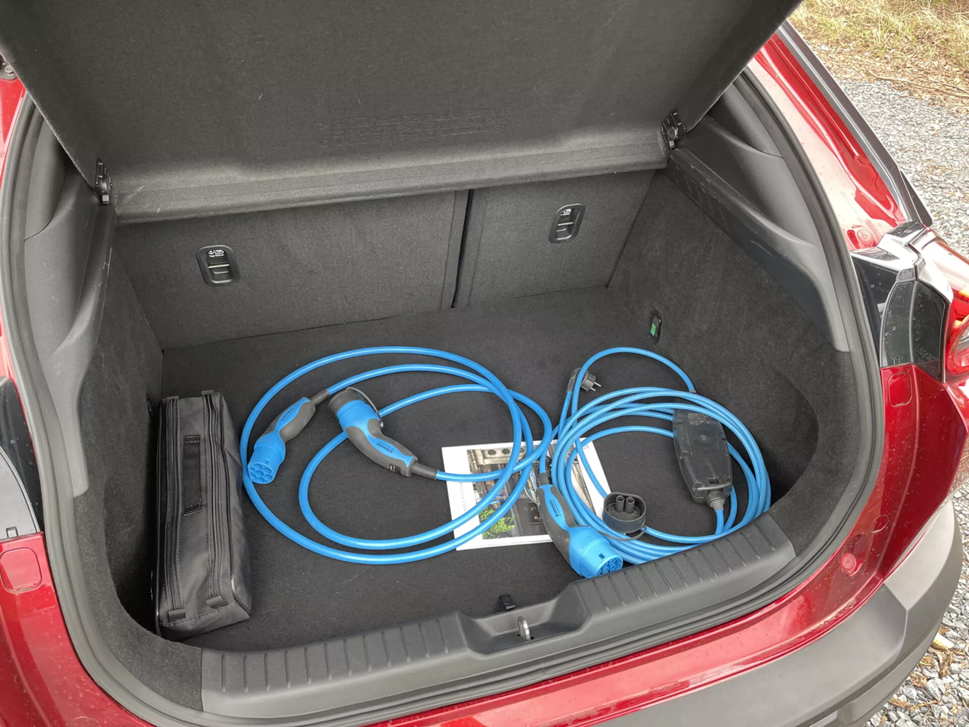Porta-malas aberto do Mazda MX-30 2020 exibindo um cabo de carregamento de veículo elétrico portátil com uma visão de perto, de cima para baixo, à esquerda, mostrando o espaço de armazenamento limpo e plano junto com compartimentos internos.