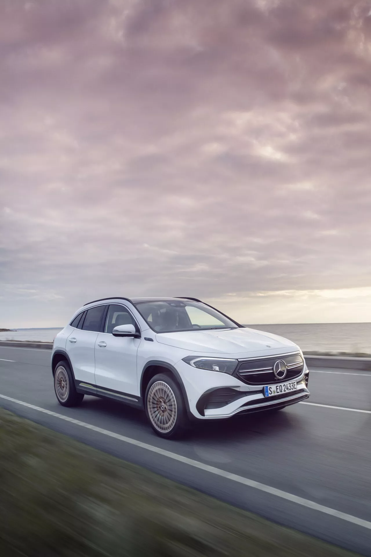 Mercedes-Benz EQA de 2021 em movimento, apresentando um ângulo frontal dinâmico de três quartos destacando o design do veículo, faróis LED, rodas de liga estilizadas e silhueta aerodinâmica contra um tranquilo pôr do sol
