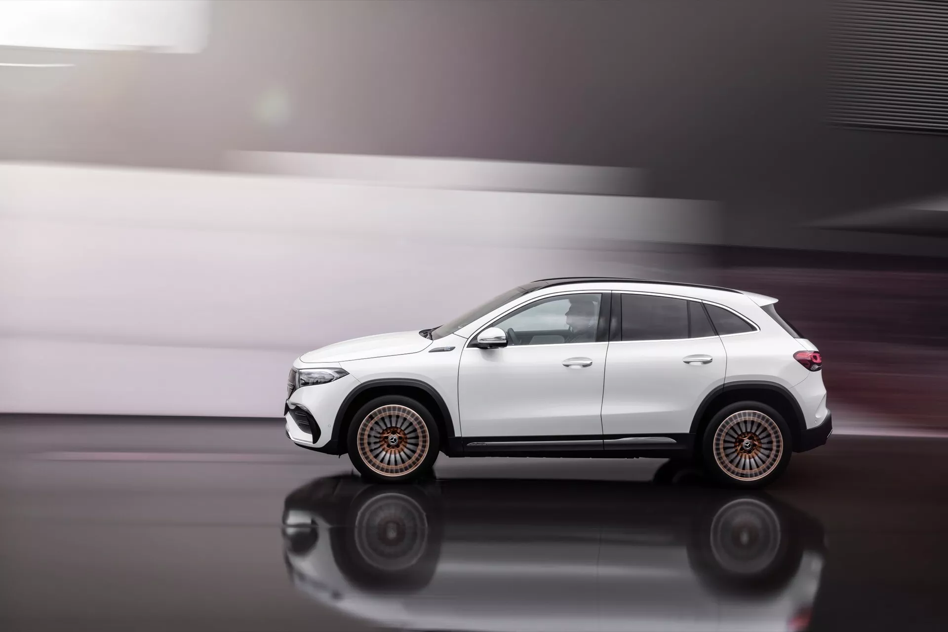 Perfil lateral dinâmico do Mercedes-Benz EQA 2021 em movimento sobre piso polido destacando rodas de múltiplos raios, espelhos dobráveis, barras de teto e linhas de carroceria esculpidas com vidros tintados de privacidade, mostrando postura off-road e potenciais recursos tecnológicos como espelhos dobráveis automáticos e antena satélite.