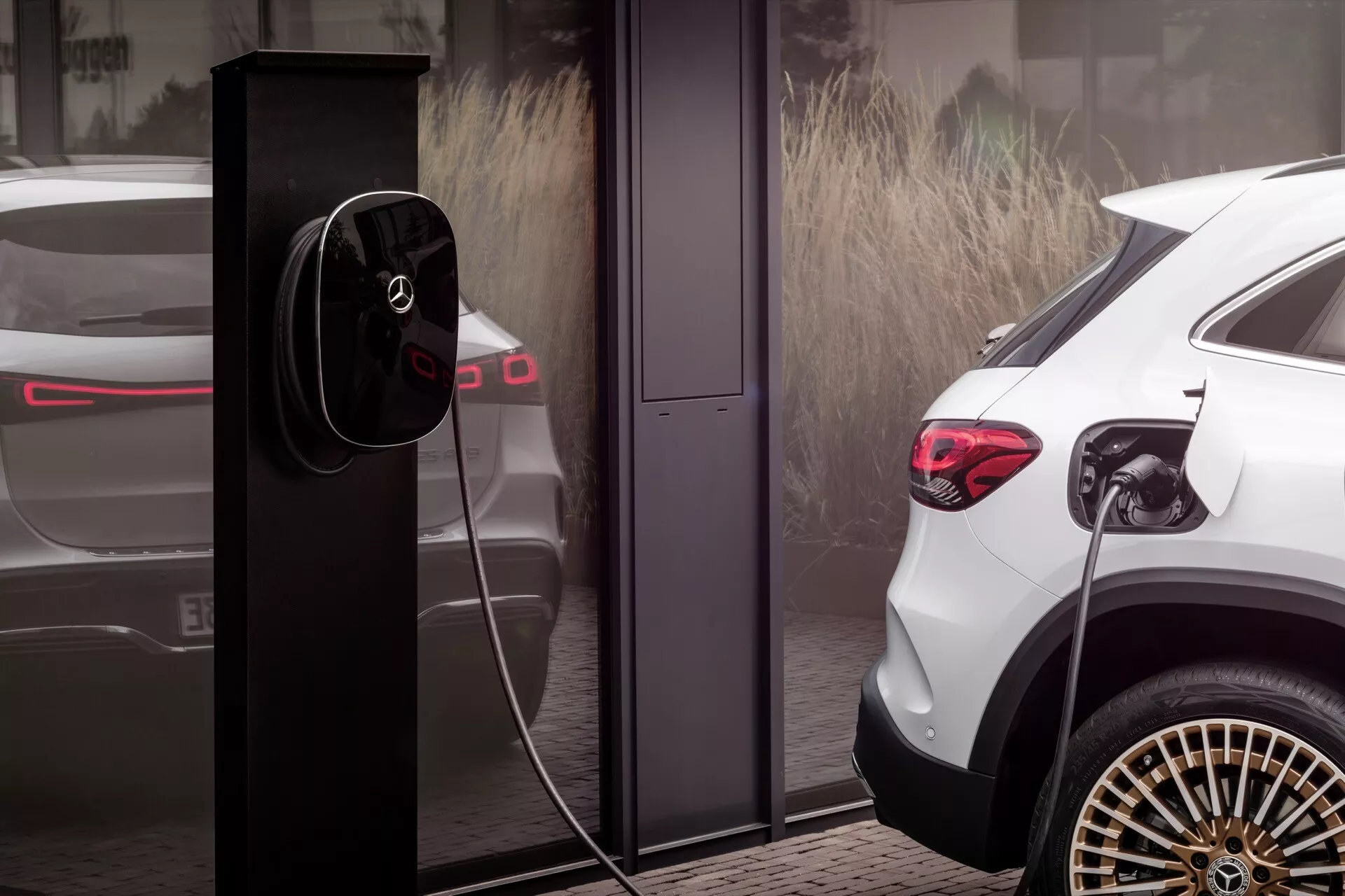SUV elétrico Mercedes-Benz EQA branco de 2021 mostrado a partir de um ângulo traseiro de três quartos, destacando sua alta distância ao solo, distintas luzes traseiras LED, elegantes rodas de liga leve multirraios e conectado a uma moderna estação de carregamento EV