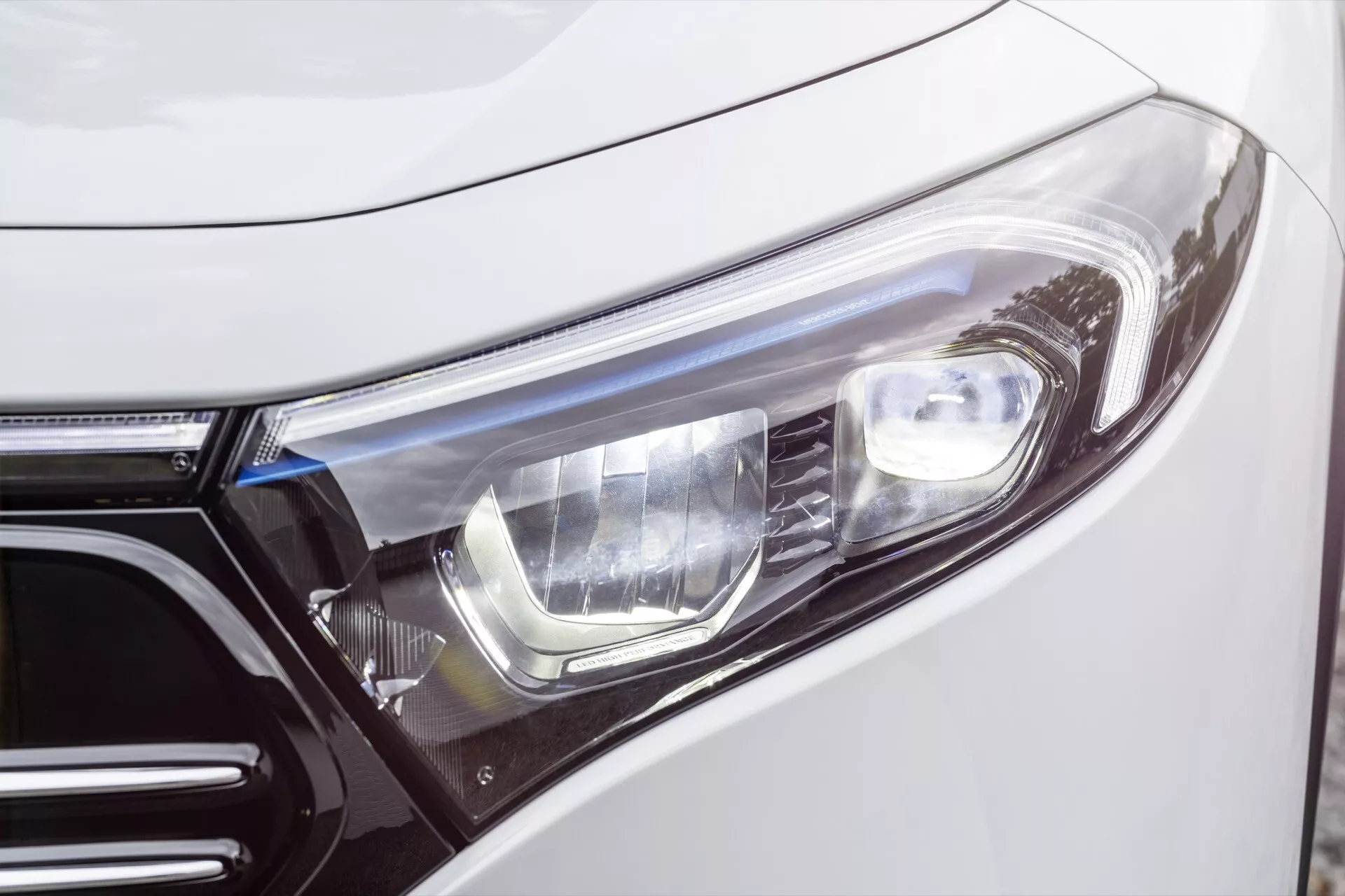 Vista de perto do lado esquerdo frontal do Mercedes-Benz EQA 2021 mostrando o design moderno do farol com foco na montagem e nos contornos de uma perspectiva ligeiramente frontal e angulada destacando a tecnologia de iluminação avançada e exterior de luxo
