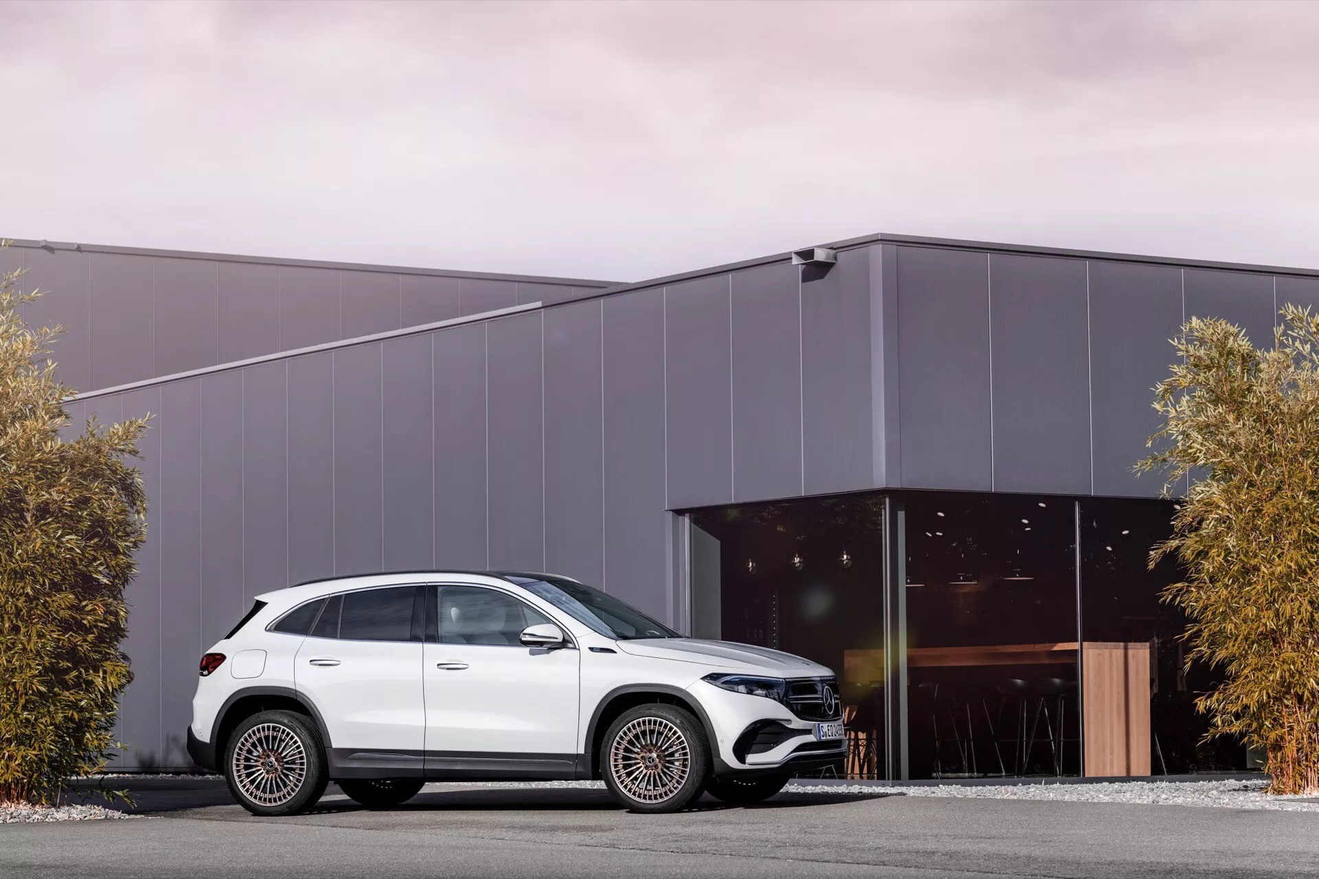 SUV branco Mercedes-Benz EQA 2021 estacionado em frente a um prédio industrial moderno, exibindo perfil lateral com visão clara da grade frontal, design dos faróis LED e rodas de liga leve esportivas à luz natural do dia