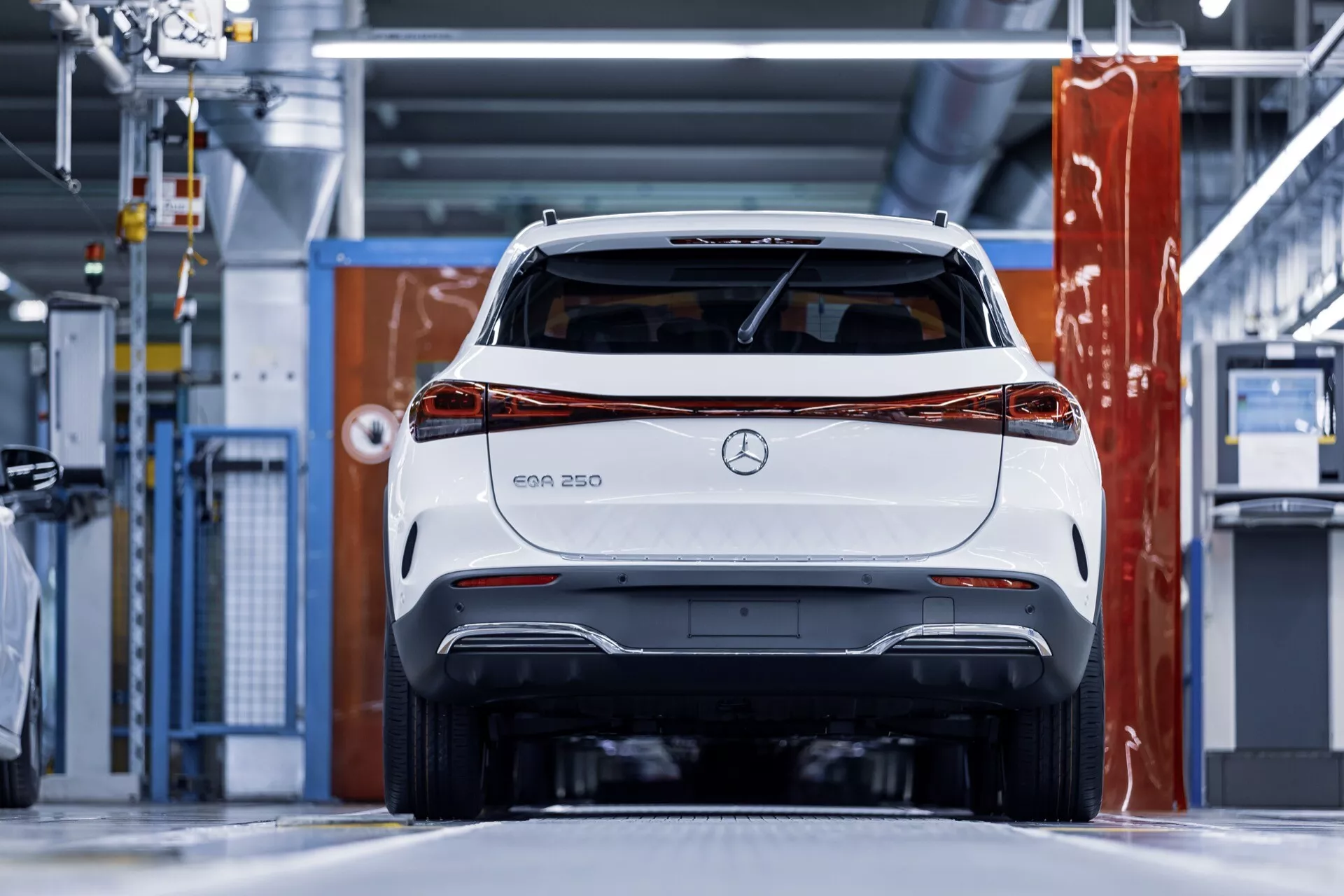 Vista traseira de um veículo elétrico Mercedes-Benz EQA 250 branco num cenário industrial moderno, destacando as luzes traseiras, o para-choque traseiro e o branding da Mercedes com um foco claro no design e características tecnológicas.
