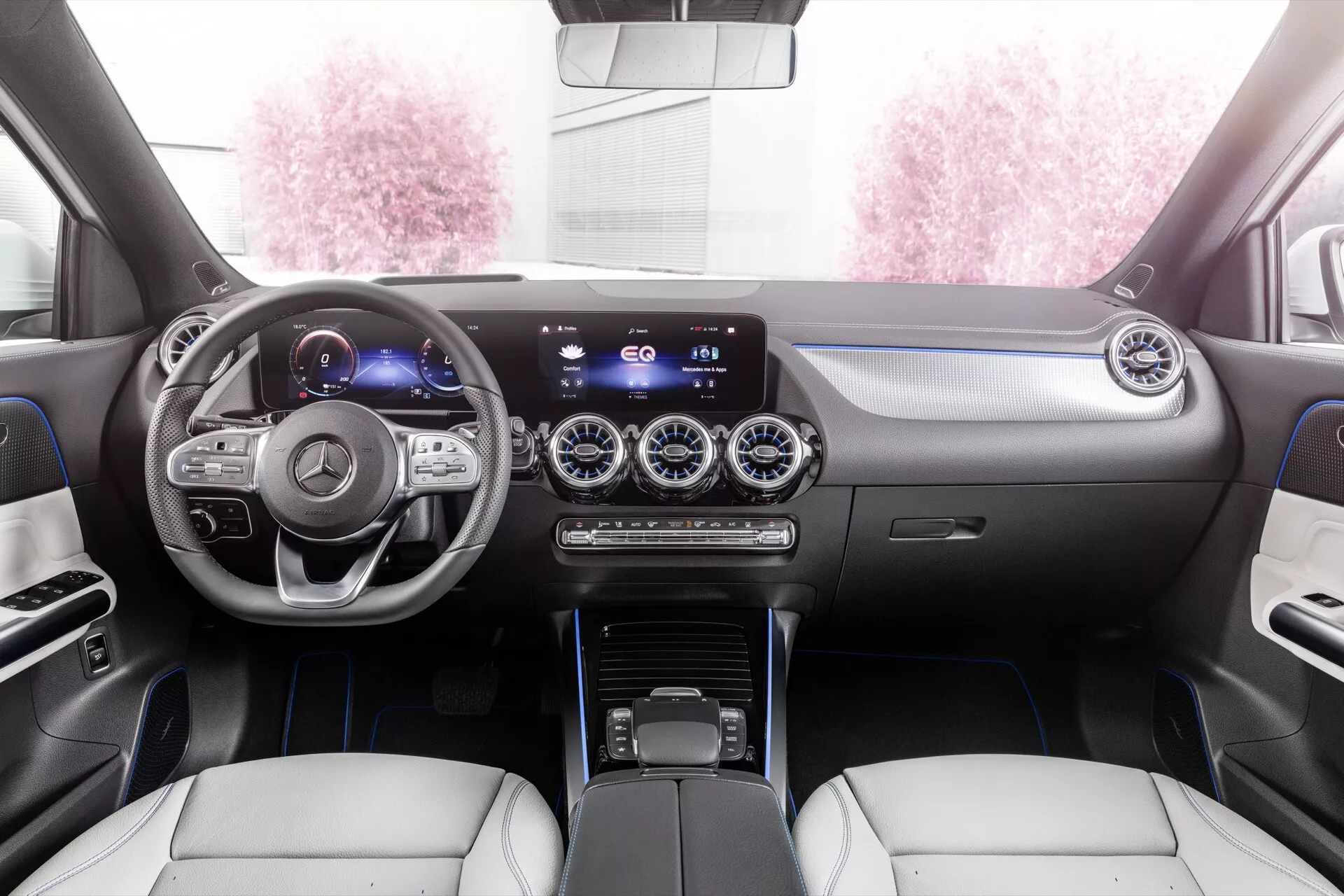 Vista interior do Mercedes-Benz EQA 2021 destacando o painel de instrumentos, volante multifuncional com detalhes em prata, cluster de instrumentos digital, sistema de infotenimento com tela widescreen, ventilação com acabamento metálico, controle de clima de duas zonas, alavanca de câmbio moderna e assentos de couro em dois tons com costuras decorativas a partir da perspectiva do assento traseiro