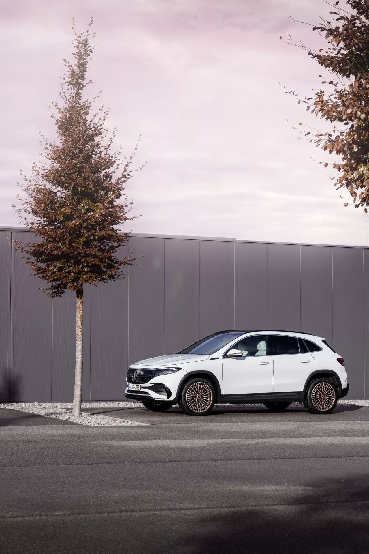 Perfil lateral do Mercedes-Benz EQA 2021 estacionado em uma rua urbana, exibindo seu design moderno de SUV com linhas fluidas, arcos de roda pronunciados, acabamento preto contrastante e rodas de liga leve de multi-raios contra um fundo nublado