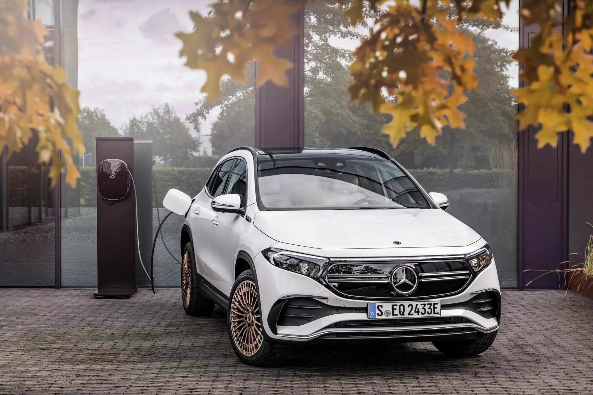 SUV de luxo branco Mercedes-Benz EQA 243 de 2021 apresentando uma visão de três quartos destacando seus faróis LED modernos, rodas de liga leve distintas e tecnologia de carregamento de veículo elétrico, cercado por um toque de folhas de outono, enfatizando seu design ecológico em um ambiente exterior luxuoso