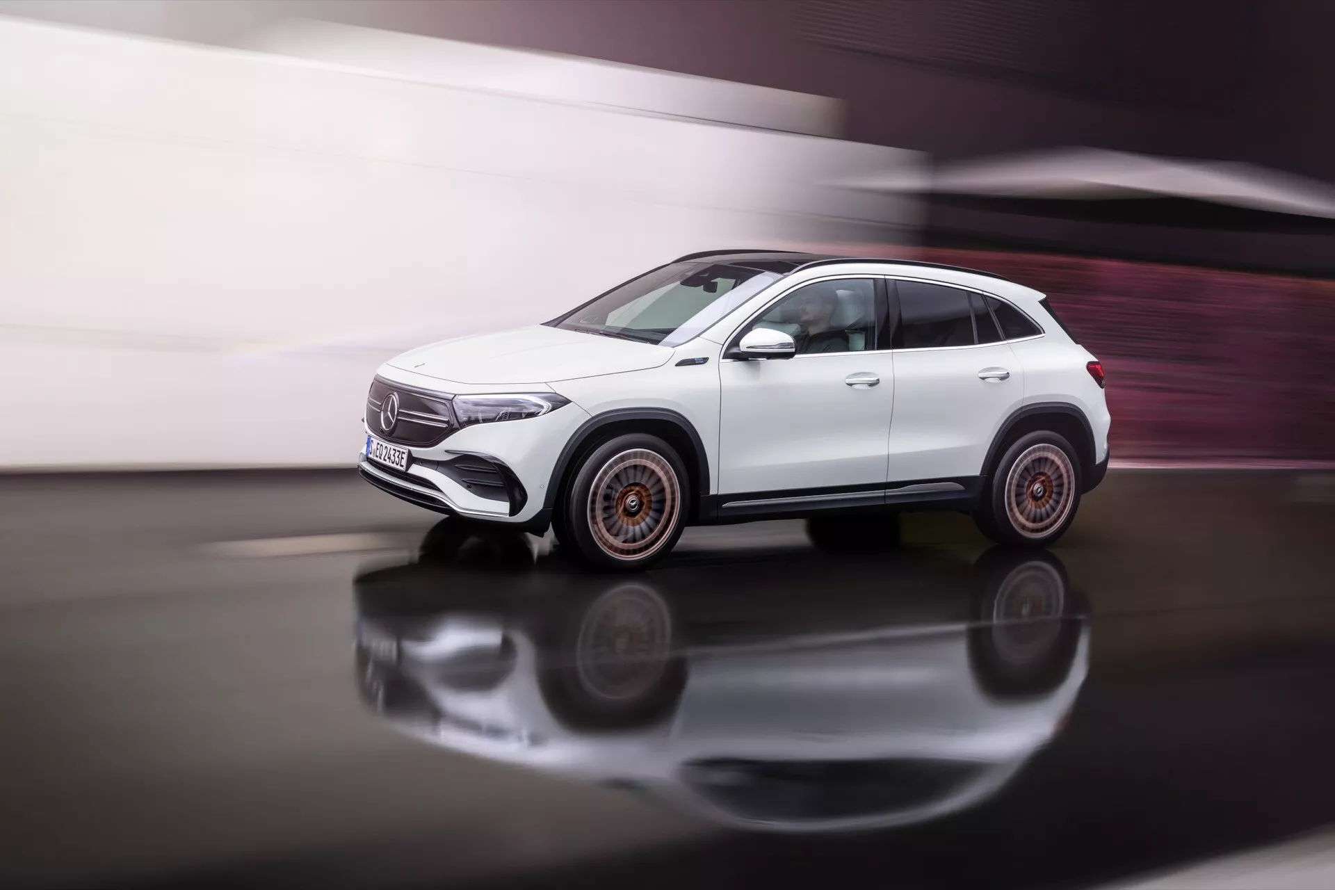 SUV branco Mercedes-Benz EQA 2021 em movimento sobre superfície reflexiva com vista lateral dinâmica destacando linhas de design, formas das janelas, portas e design único das rodas com leve desfoque de movimento e acentos cor de cobre