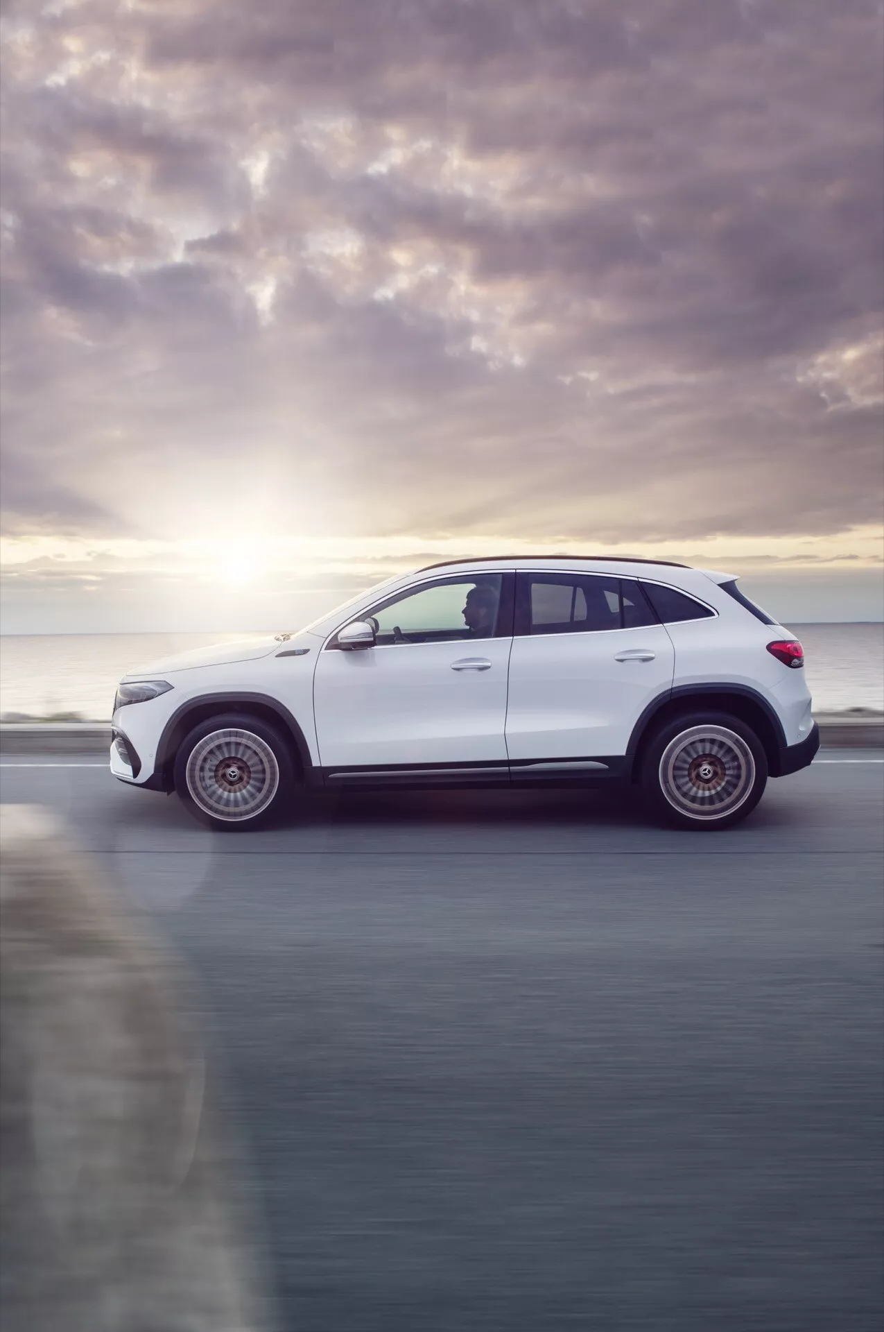 Vista lateral do SUV branco Mercedes-Benz EQA 2021 mostrando desfoque de movimento, capturada ao nascer ou pôr do sol com foco nas características de design e tecnologia moderna.