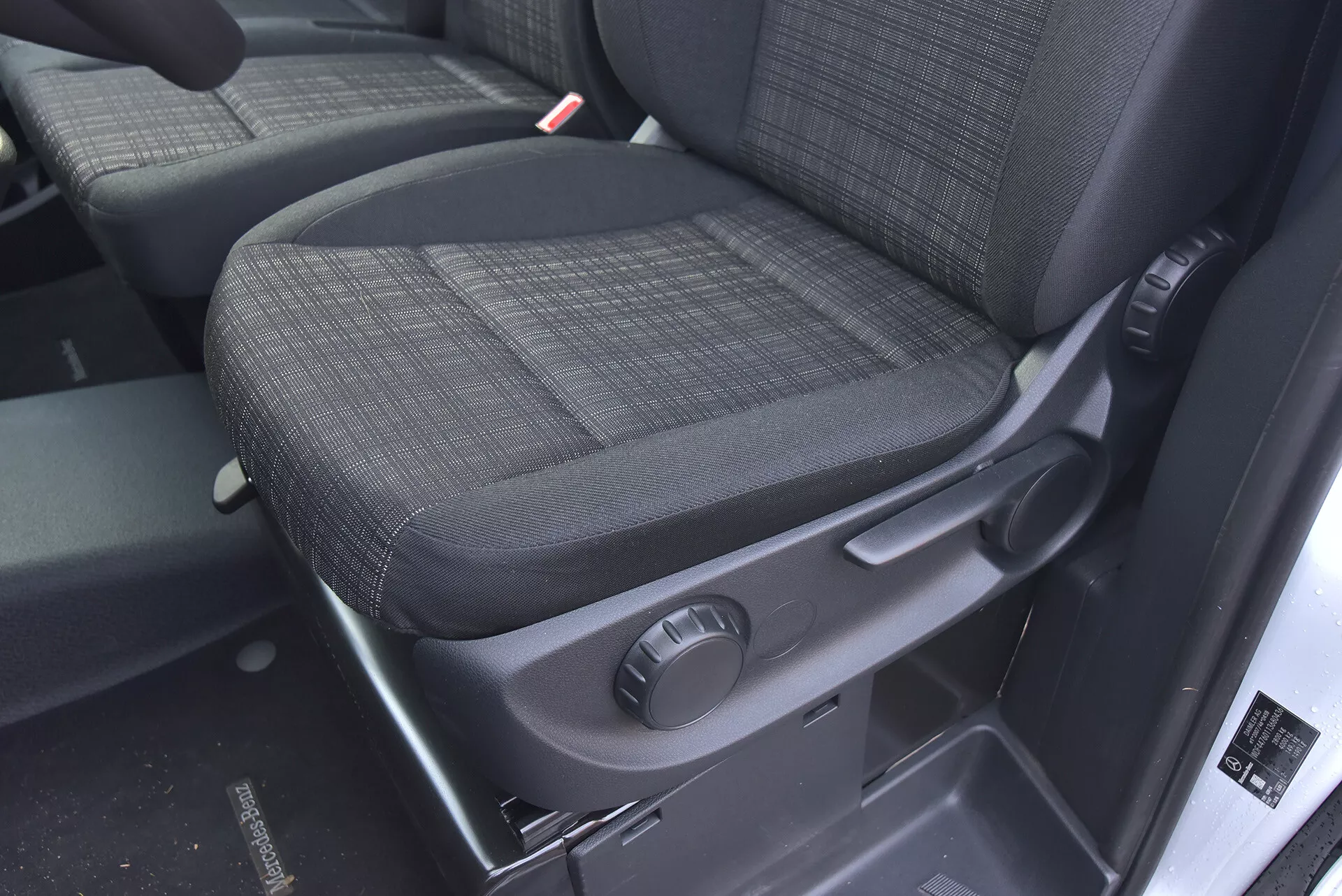 Interior do Mercedes-Benz Vito 2014 Tourer focado no assento do passageiro com estofamento de tecido escuro durável, botão de ajuste manual e recursos de segurança como o receptor do cinto de segurança claramente visível.