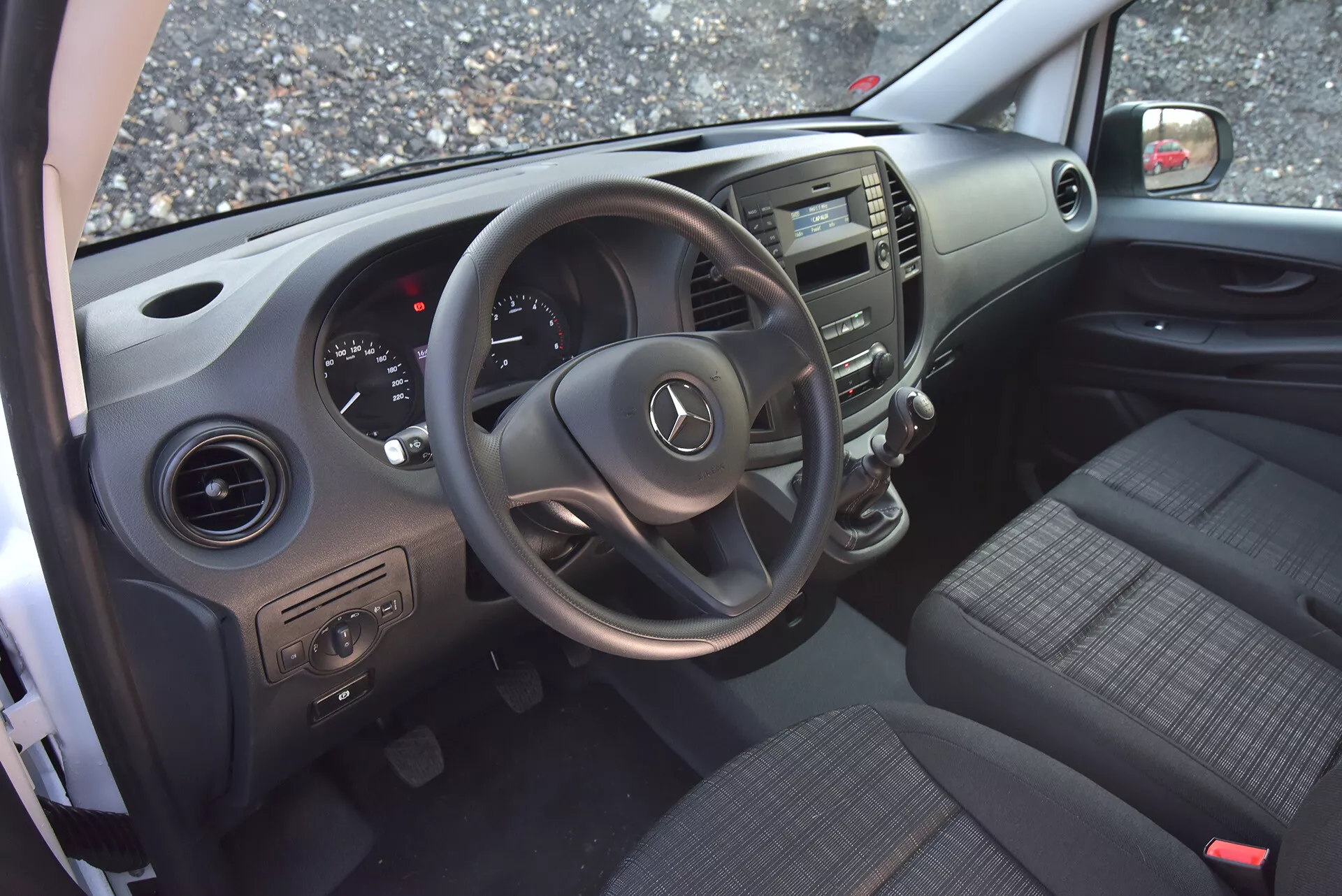 Interior da Mercedes-Benz Vito Tourer de 2014 visto de uma porta do lado do condutor aberta, destacando o volante com logótipo da Mercedes, painel de instrumentos, consola central, assentos de tecido, controles na porta e saídas de ar.