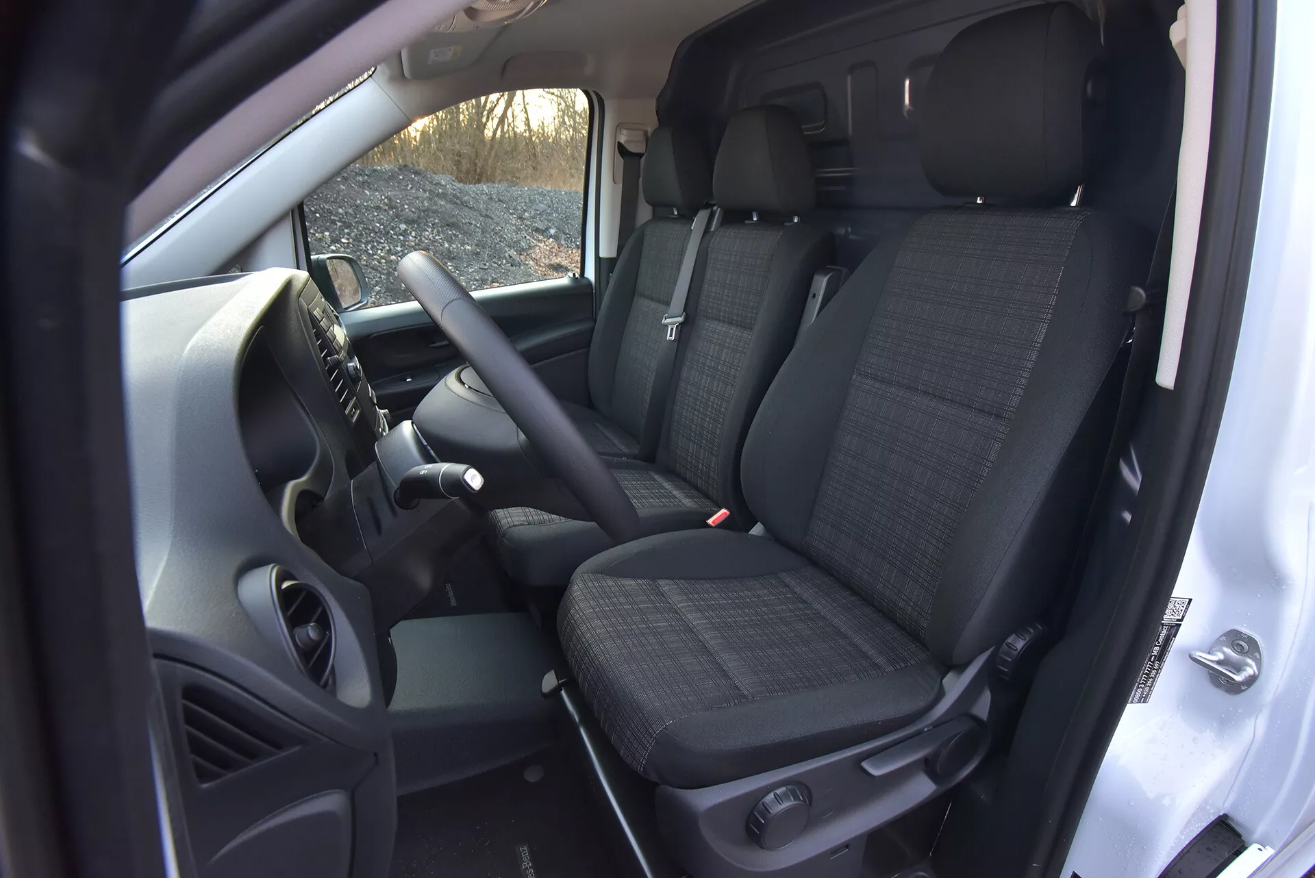Vista interior do Mercedes-Benz Vito 2014 (Vito-Tourer) mostrando a área do motorista e do passageiro da frente com características tecnológicas como controles montados no volante, um console central que potencialmente abriga um sistema de infotenimento, assentos dianteiros com tecido estampado e apoios de cabeça, e uma visão parcial dos assentos traseiros, tudo capturado de um ângulo alto destacando a espaçosidade da cabine e elementos de transmissão manual.