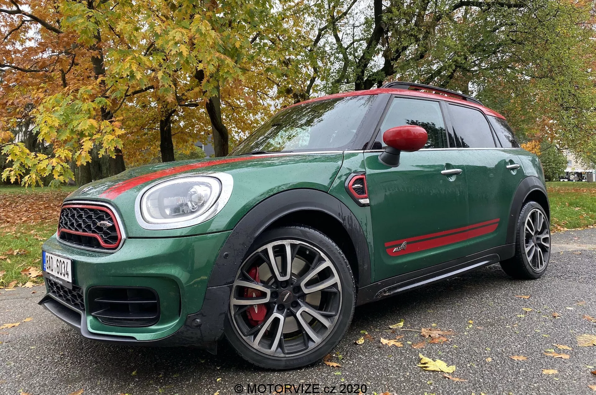 Vista frontal de três quartos em ângulo baixo de um Mini Countryman John Cooper Works 2020, mostrando seu exterior verde escuro com detalhes em vermelho, rodas esportivas de múltiplos raios, grade com moldura cromada, grandes entradas de ar, faróis de LED e pinças de freio vermelhas.