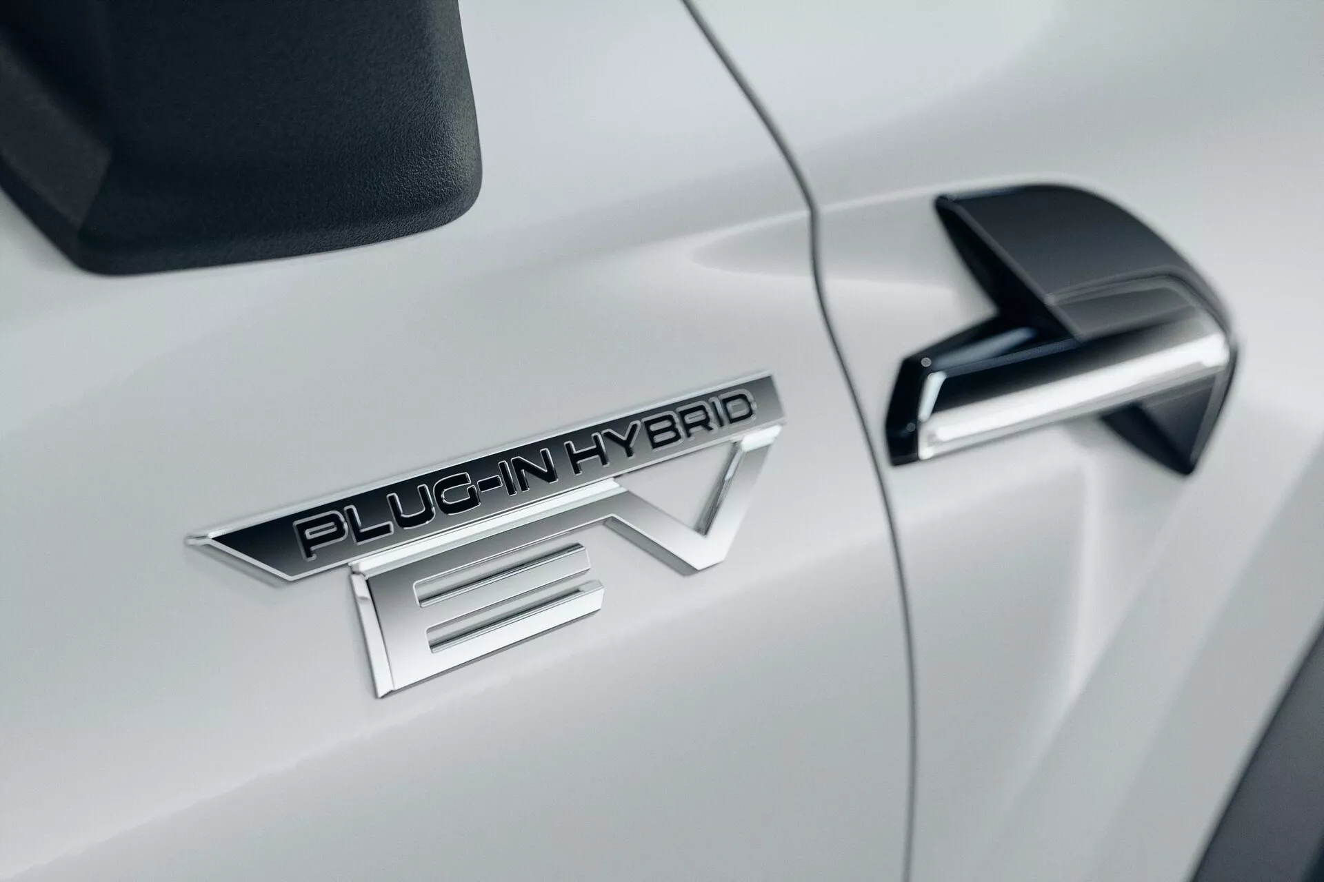 Close-up do lado do carro branco Mitsubishi ASX 2023 de segunda geração, com o distintivo proeminente 'PLUG-IN HYBRID EV', elegante retrovisor lateral preto com sinal de seta integrado e carroceria aerodinâmica branca brilhante.