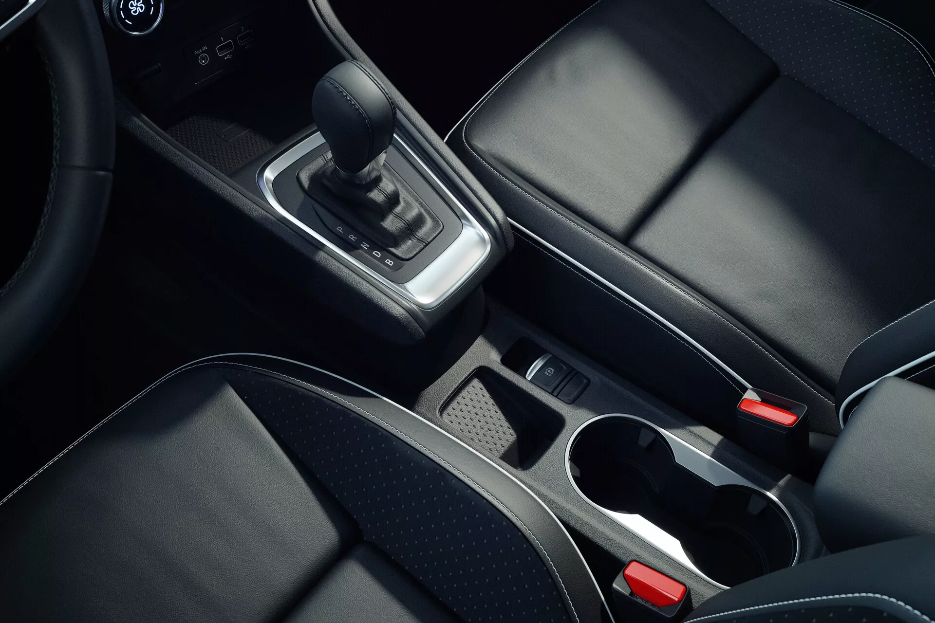 Imagem do interior do console central do Mitsubishi ASX 2023 segunda geração, tomada de um ângulo superior, focando em detalhes como a alavanca de câmbio de couro, acentos cromados ao redor da área de câmbio, compartimento de armazenamento com bandeja removível, dois porta-copos com bordas cromadas, assentos de couro preto com costura visível, botão de freio de estacionamento eletrônico e apoio de braço central parcialmente visível, mostrando materiais de alta qualidade e design moderno.