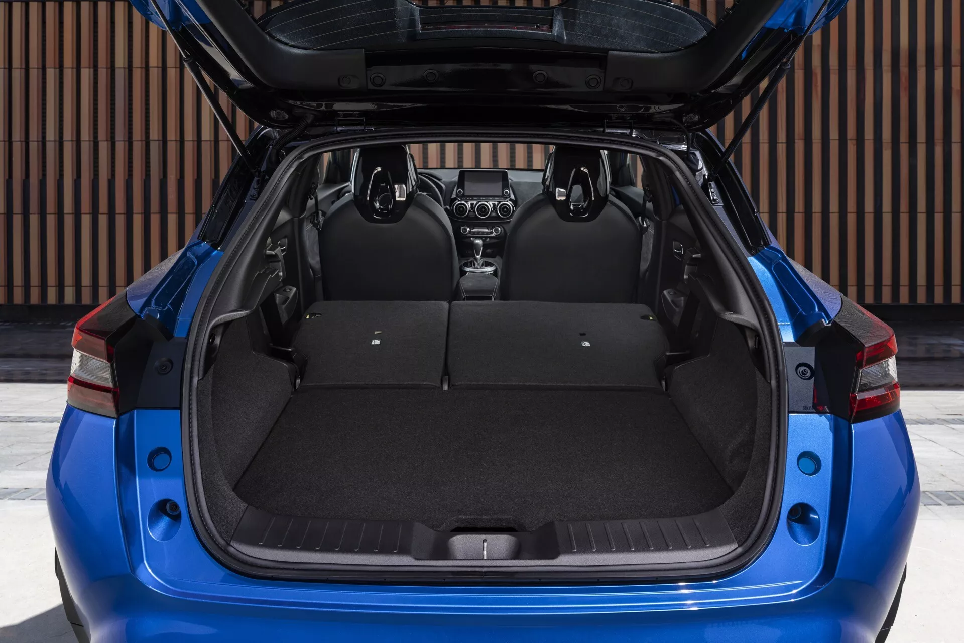 Nissan Juke F16 de 2019 em azul, vista traseira com porta-malas aberto mostrando área de carga espaçosa, bancos traseiros rebatíveis divididos, e cobertura de carga retrátil visível
