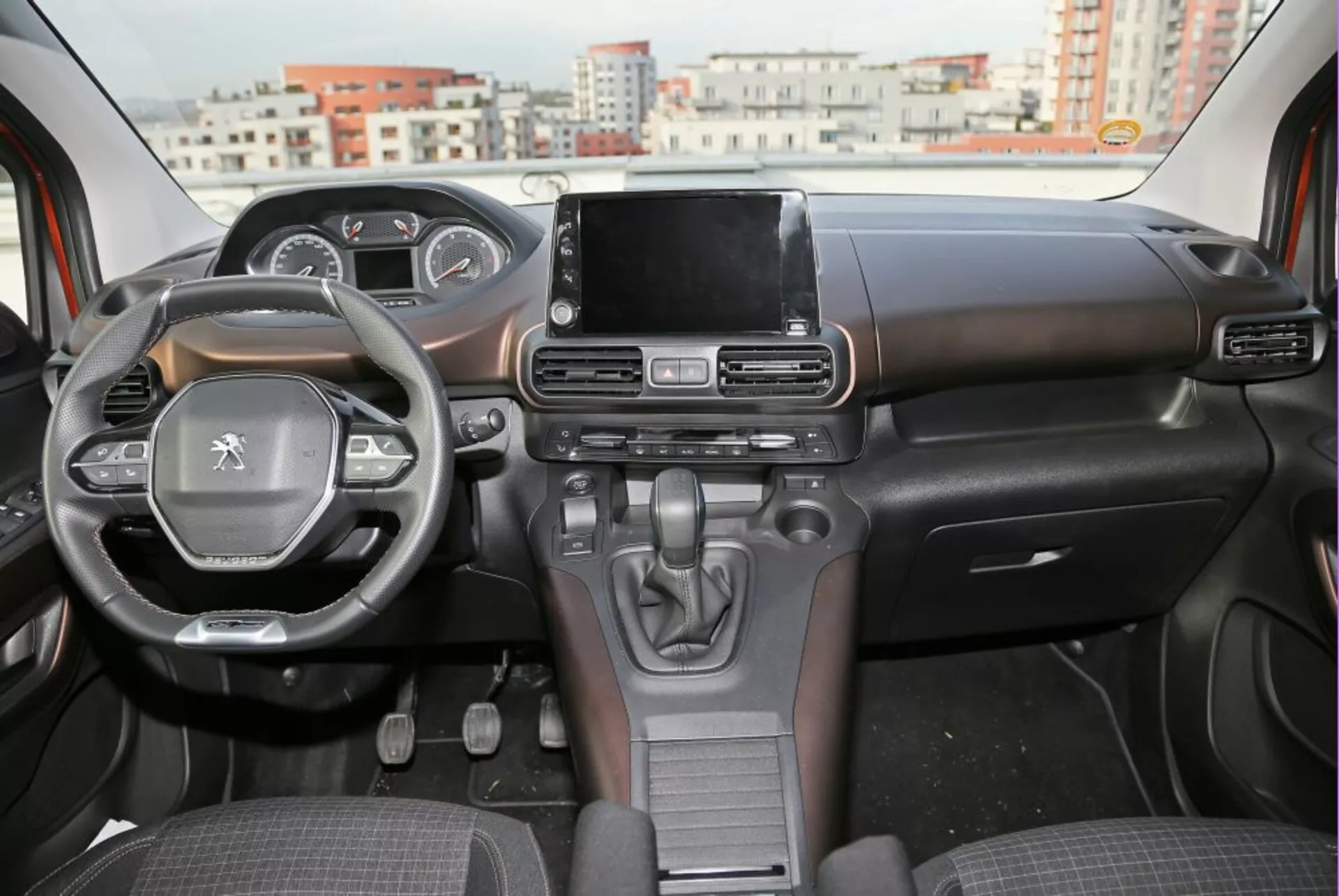 Vista interior de um Peugeot 3008 de 2016 mostrando o painel de instrumentos, volante com controles montados, e tela sensível ao toque central do sistema de entretenimento a partir da perspectiva do assento traseiro