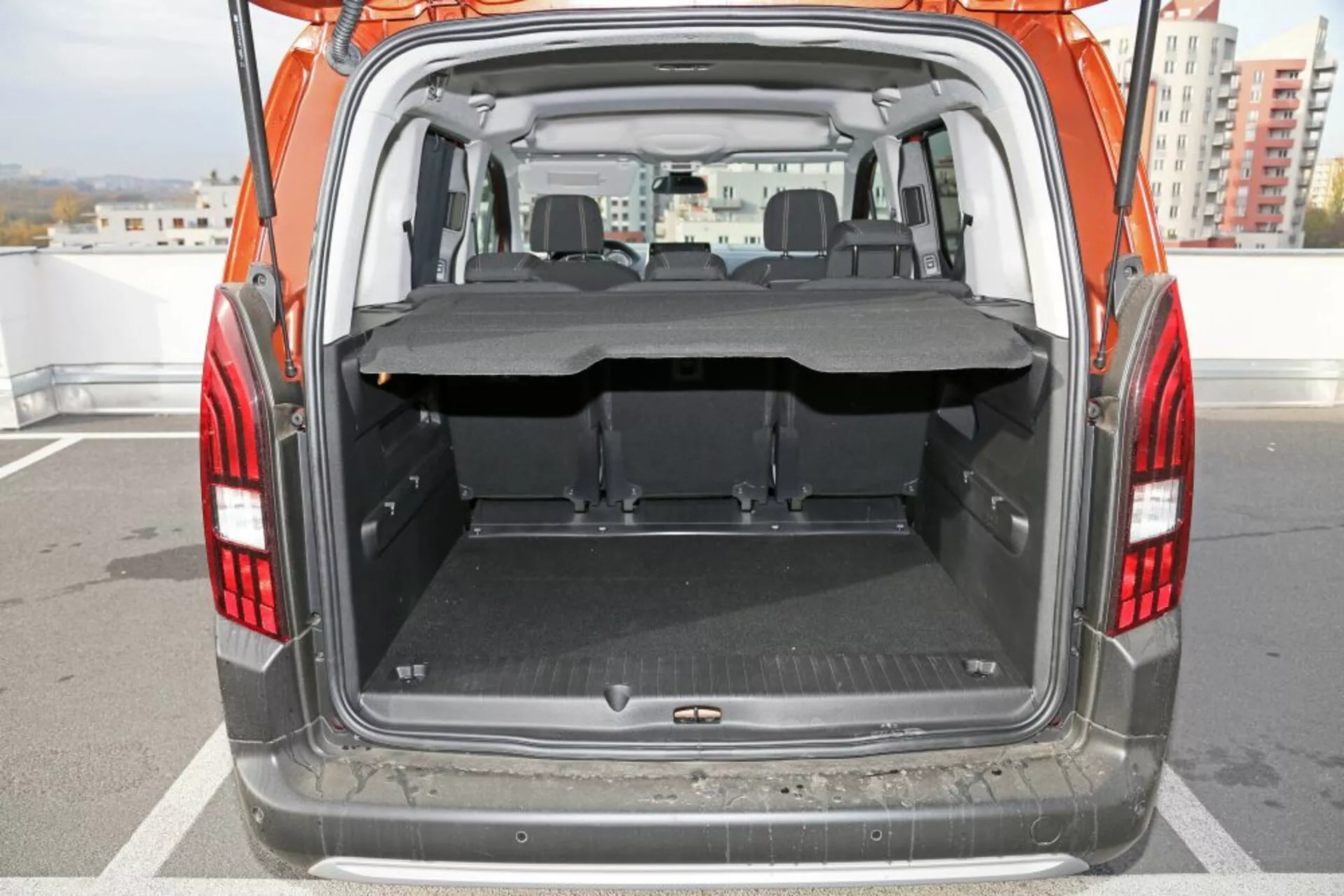 Vista traseira de um SUV Peugeot 3008 de 2016 focando no porta-malas aberto e na área de carga, apresentando um piso limpo e plano com um tapete protetor, cobertura de carga parcialmente estendida, bancos traseiros dobráveis, e visibilidade clara para a área de assentos da frente através da parte de trás.
