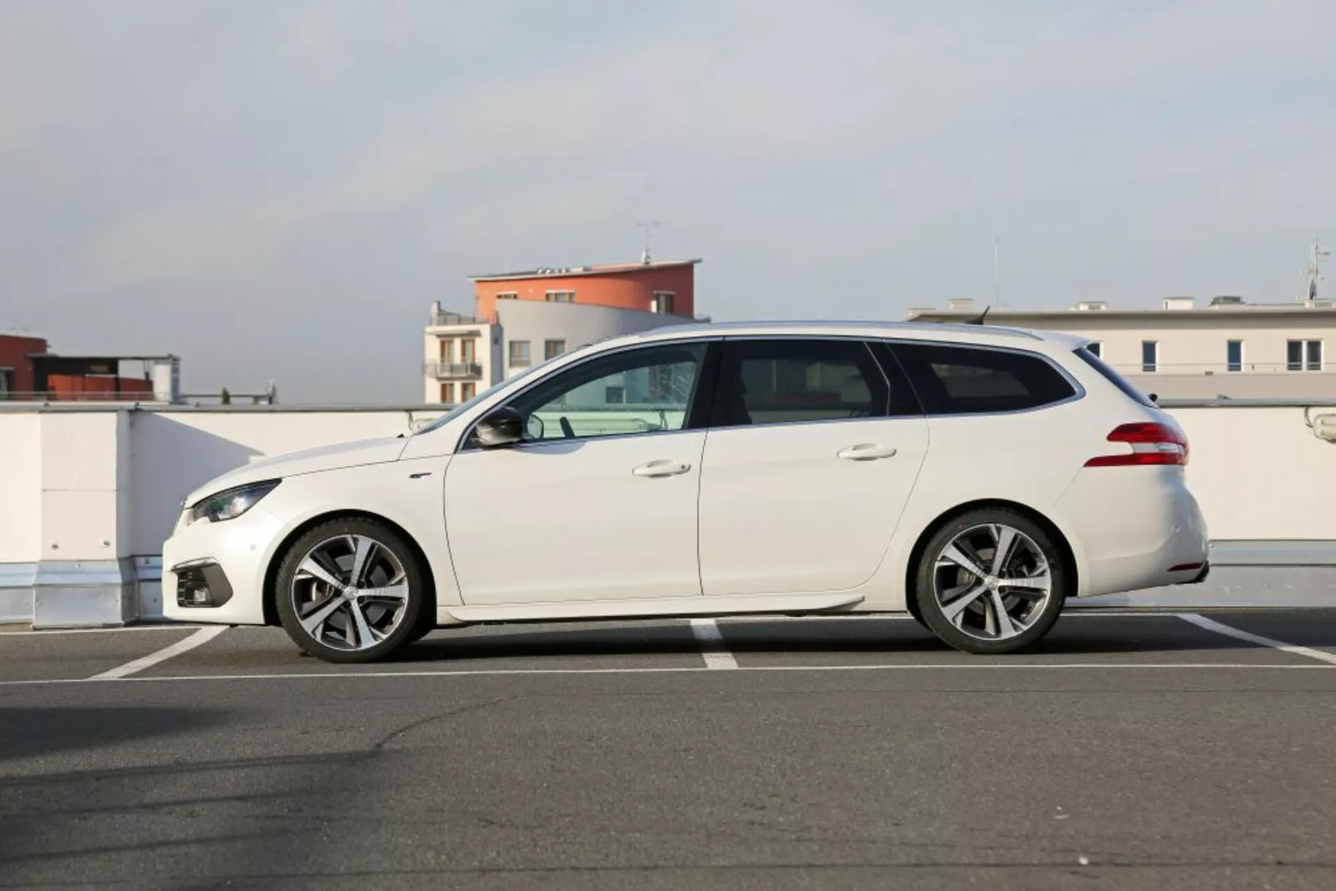 Station wagon Peugeot 3008 branco de 2016 estacionado no asfalto, vista lateral de perfil mostrando faróis elegantes, rodas de liga leve com múltiplos braços, espelhos laterais na cor da carroceria e cinco portas