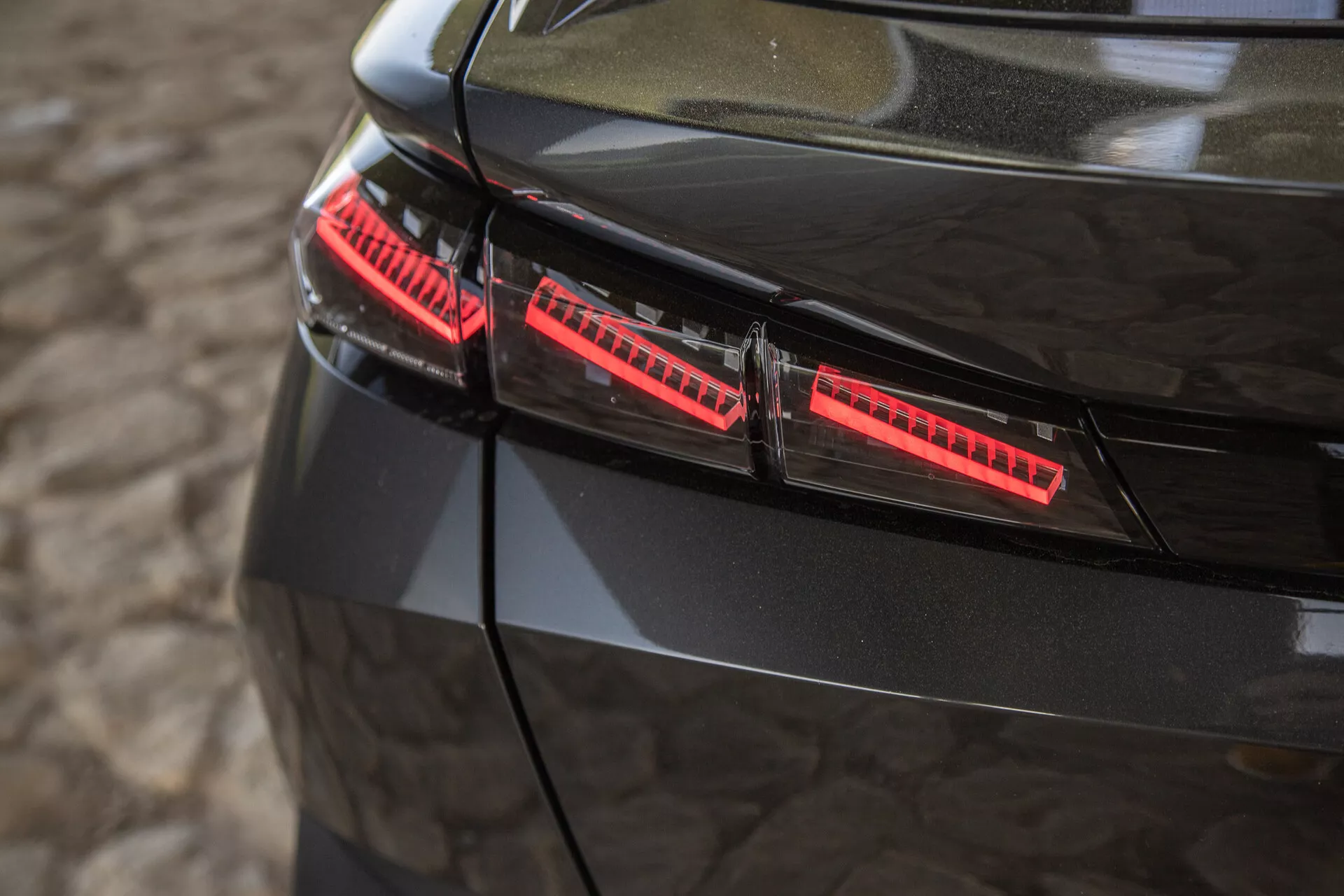 Vista de perto das luzes traseiras pretas brilhantes do Peugeot 408 2023, com elementos LED modernos e elegantes detalhes de design capturados de um ângulo elevado