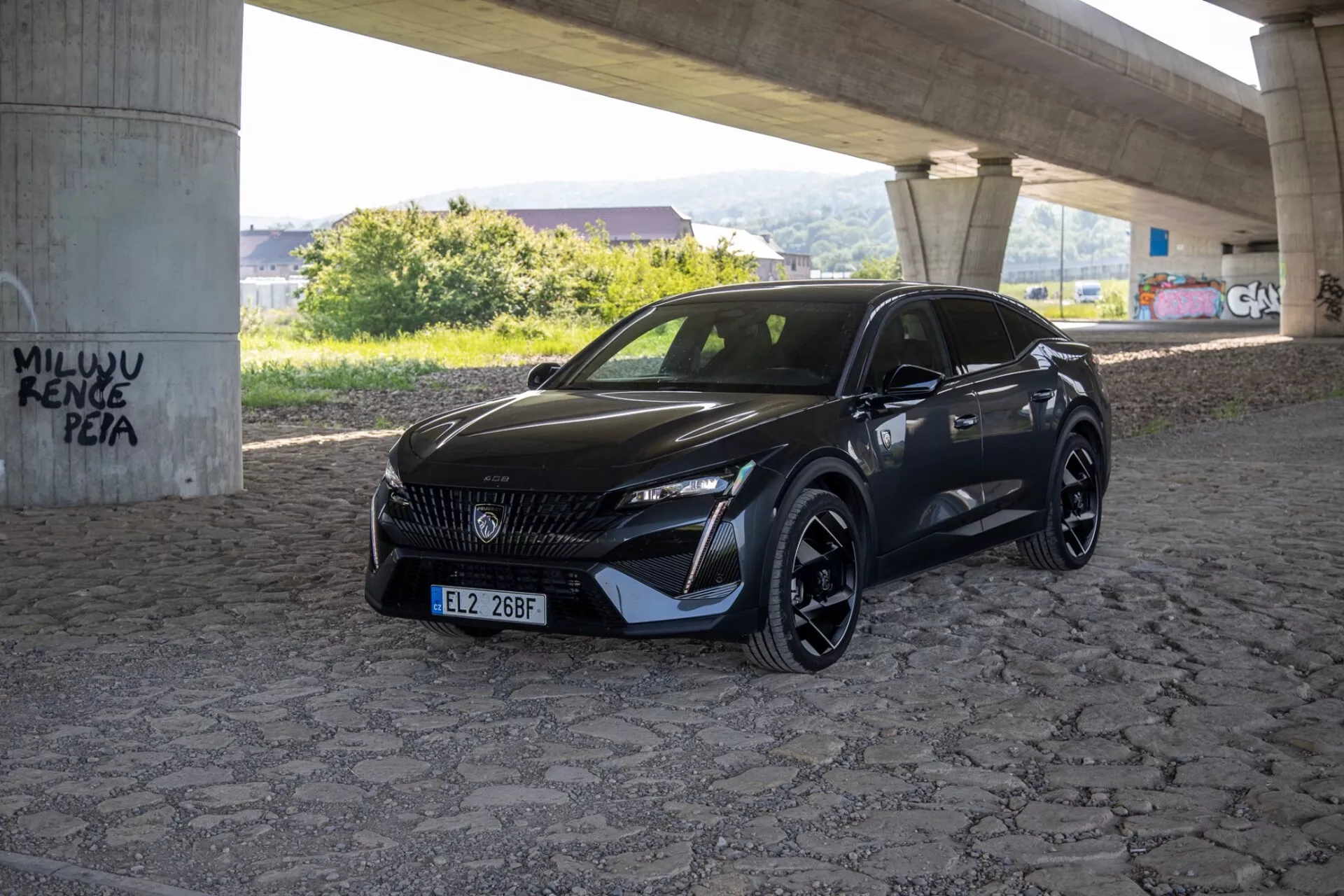 Peugeot 408 2023 capturado de um ângulo de três quartos destacando seus faróis LED elegantes, grade padronizada e para-choque dianteiro esportivo aerodinâmico sob luz natural do dia em uma área pavimentada sob um viaduto