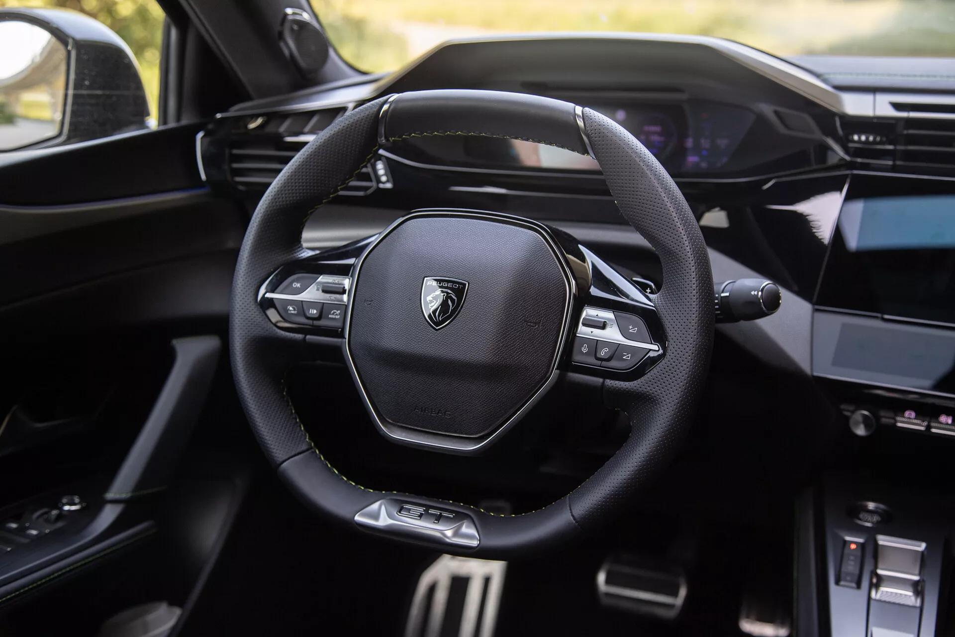 Interior do Peugeot 408 2023 mostrando volante moderno multifuncional com logotipo de marca, painel digital ao fundo e console central parcialmente visível com sistema de infotenimento
