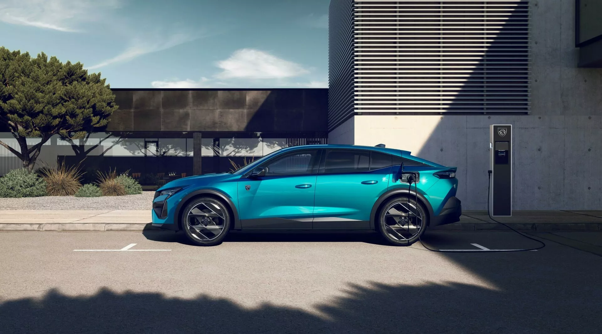 Veículo elétrico Peugeot 408 de 2023 em azul metálico estacionado em estação de carregamento externo, mostrando rodas de liga leve esportivas de cinco pontas, silhueta aerodinâmica, maçanetas de portas embutidas, porta de carregamento visível, espelhos laterais convencionais, janelas com privacidade tintadas e teto solar panorâmico sob condições de luz do dia brilhante com arquitetura moderna ao fundo