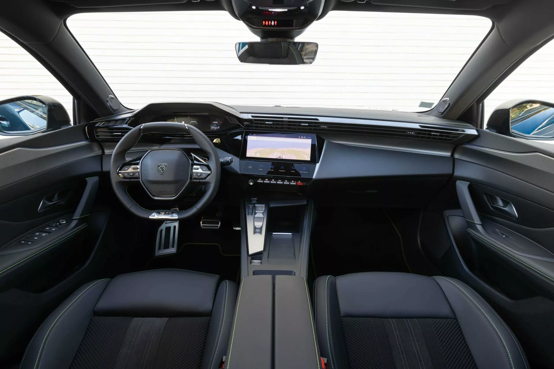 Vista interior do Peugeot 408 2023 a partir da área de assentos traseiros destacando o painel de instrumentos, volante multifuncional com emblema da marca e sistema de infotenimento avançado
