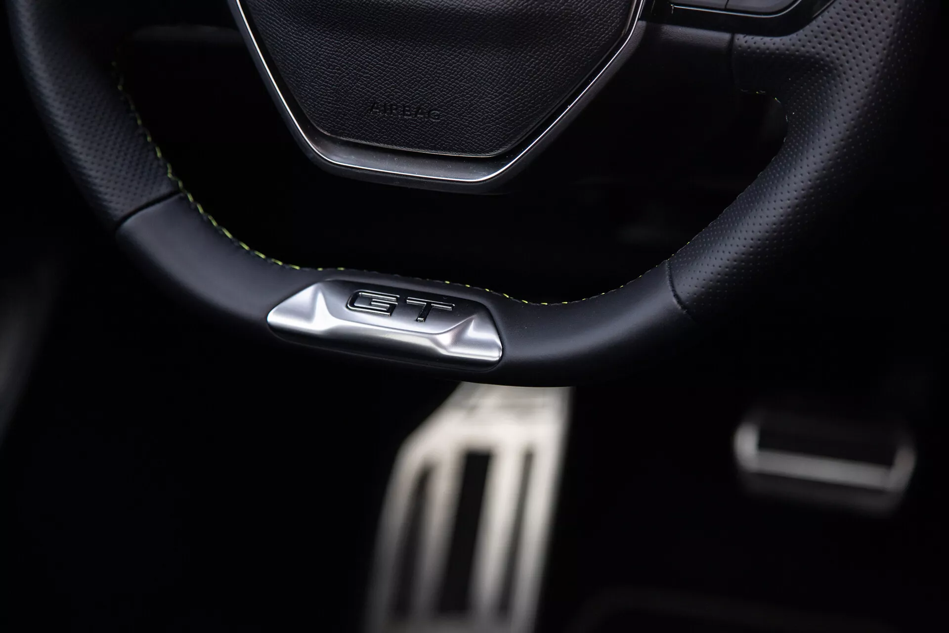 Interior do Peugeot 408 2023 focado no volante esportivo com costura de couro e emblema GT, pedais metálicos de alto desempenho e características premium do cockpit escuro