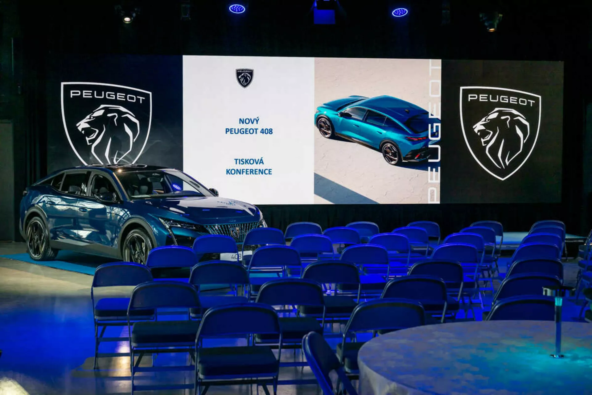 Peugeot 408 exibido em uma conferência de imprensa, visto em um ângulo de 45 graus destacando seus perfis frontal e lateral, design elegante e faróis LED, com telas digitais e branding ao fundo