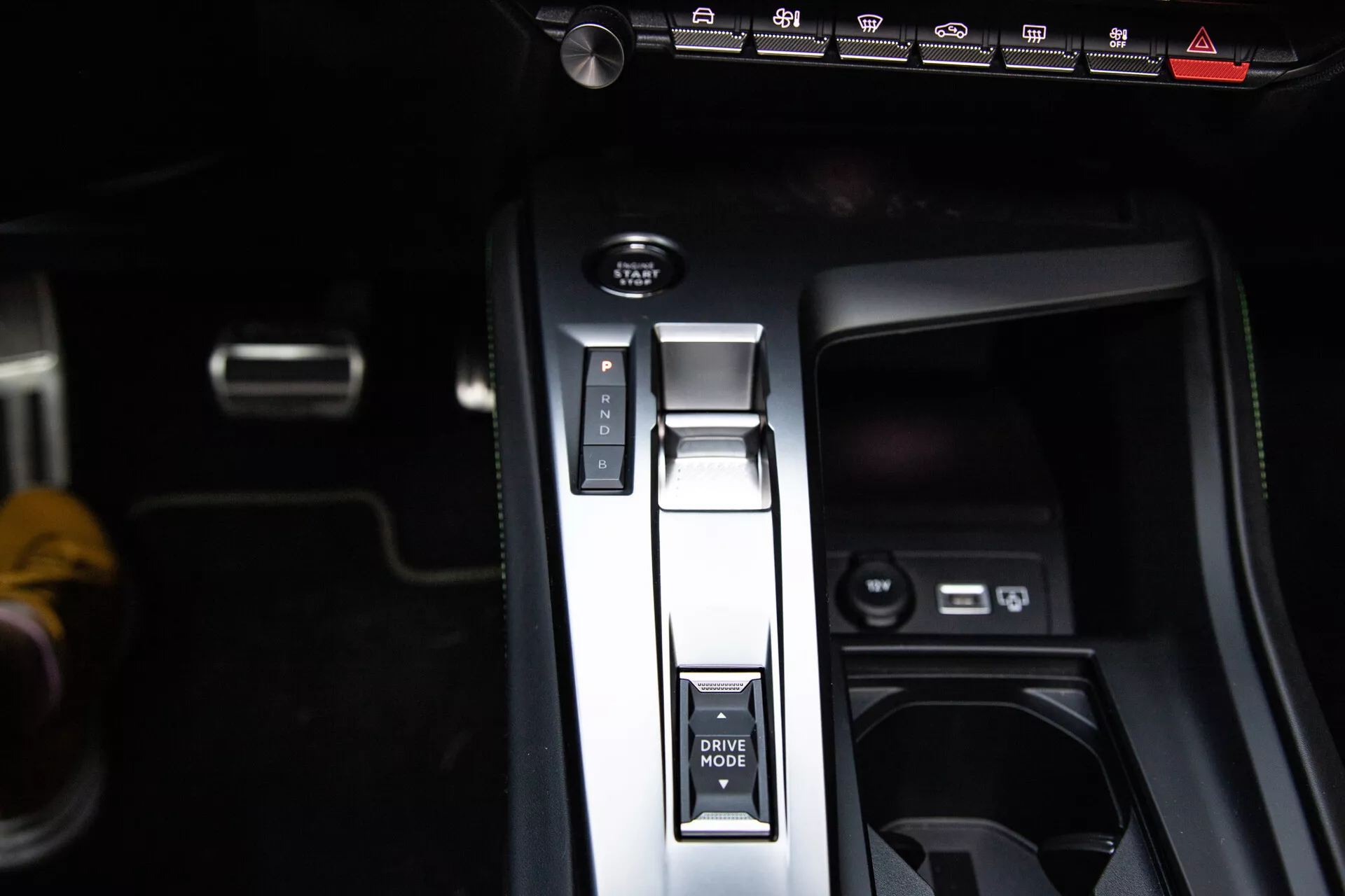 Vista de perto do console central do Peugeot 408 2023 com alavanca de câmbio na posição Parque, botão MODO DE CONDUÇÃO, freio de estacionamento eletrônico e portas USB, exibindo um design interior moderno.