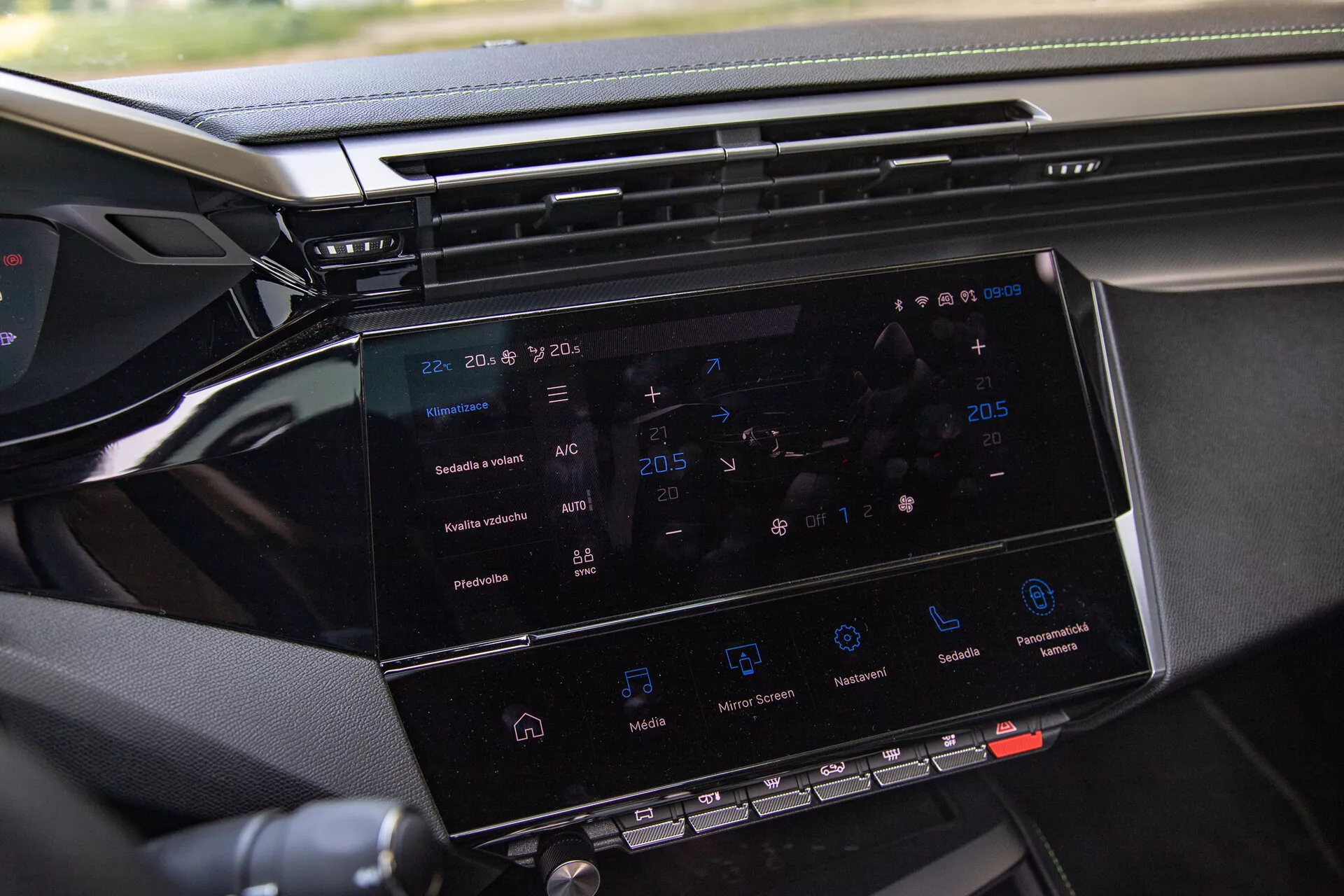 Visão detalhada do sistema de infotainment do Peugeot 408 2023 exibindo uma tela de toque de 8-10 polegadas com navegação, controle de clima, ícones de reprodução de mídia e visão parcial do painel, tirada do lado do passageiro