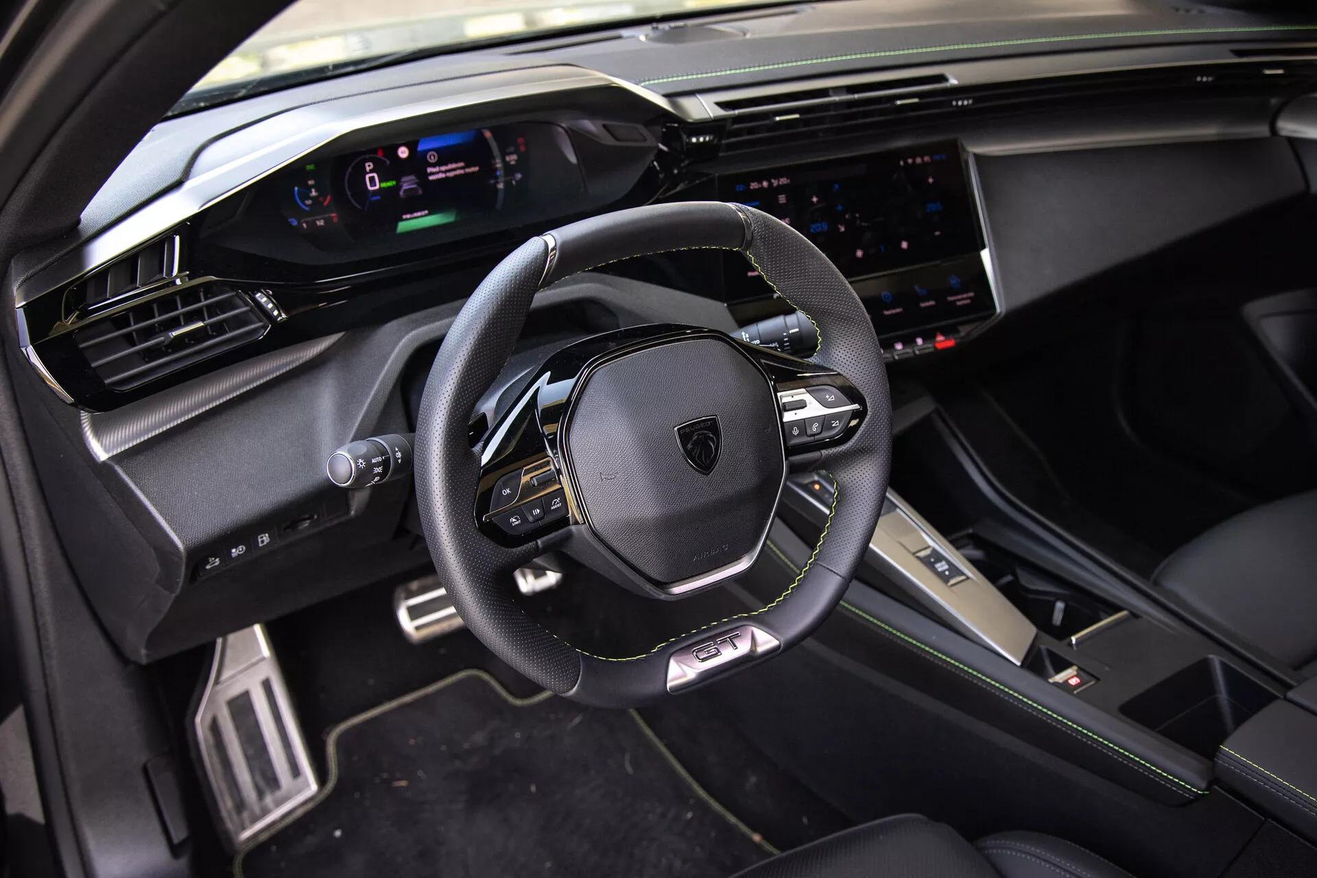 Interior do Peugeot 408 2023 exibindo um volante multifuncional revestido em couro, um cluster de instrumentos digitais, um sistema de infotainment touchscreen amplo e elementos de design esportivo premium sob luz natural do ponto de vista do passageiro dianteiro.