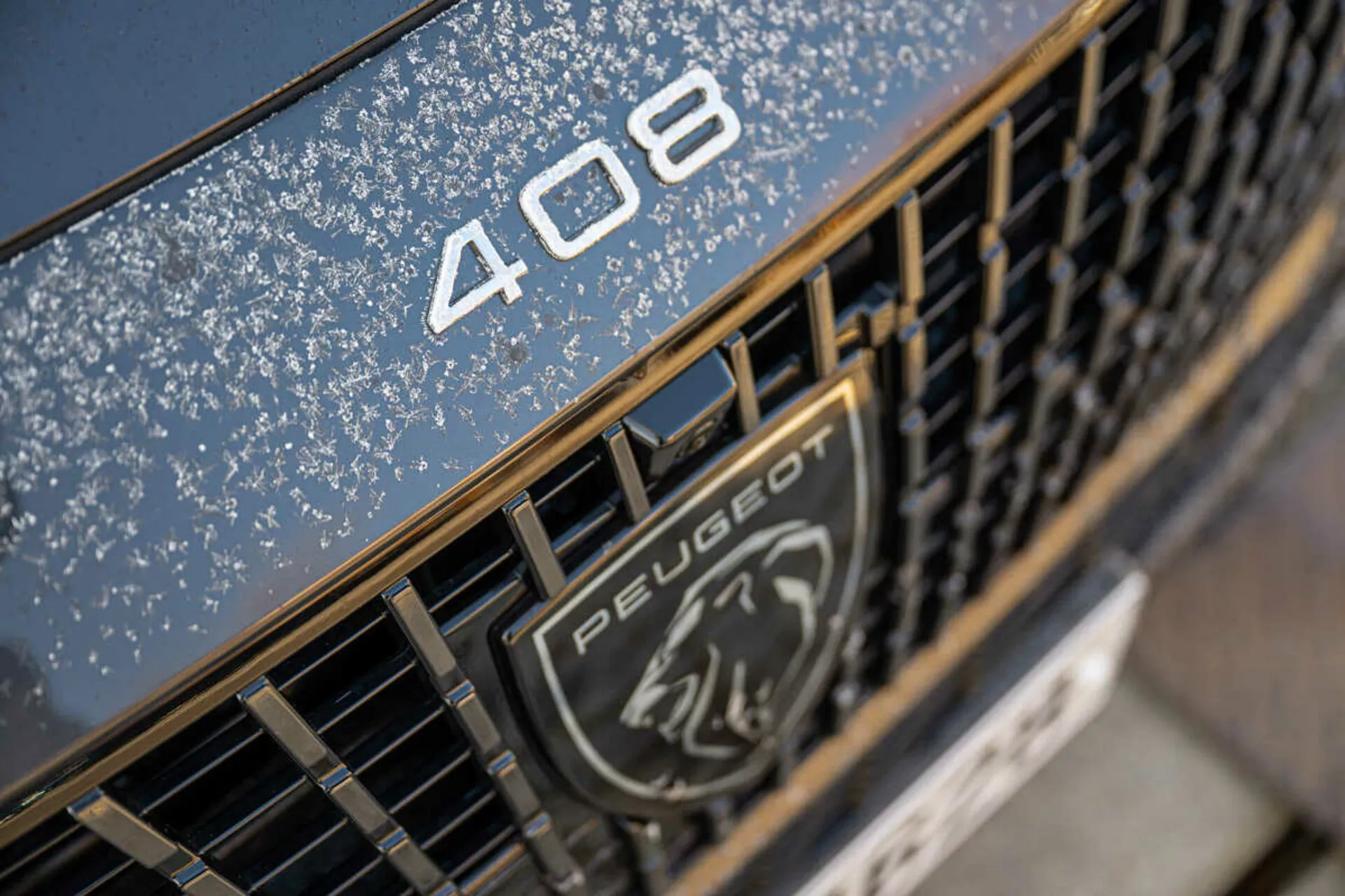 Vista de perto da designação do modelo Peugeot 408 2023 na grade com emblema e reflexo do céu noturno