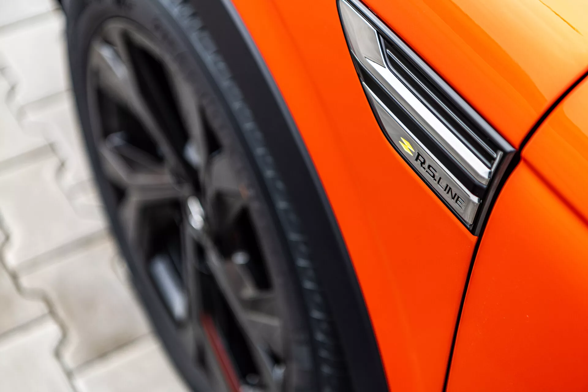 Vista de perto de um Renault Arkana laranja de 2021 exibindo o perfil lateral com foco no emblema S-Line, para-lama e design esportivo da roda de um ângulo baixo