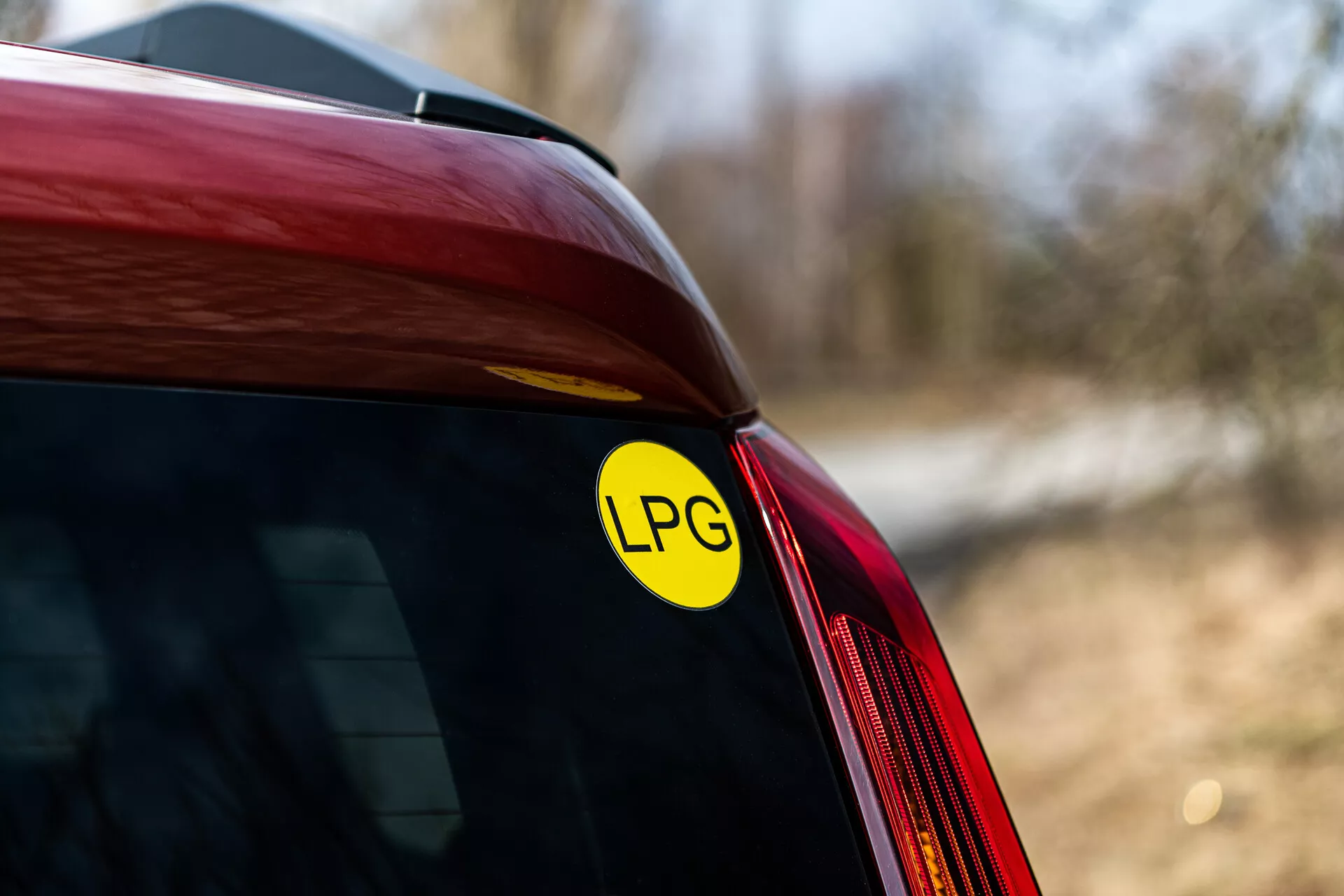 Close-up do canto traseiro de um Renault Arkana vermelho de 2021 exibindo o adesivo de GLP para capacidade de gás de petróleo liquefeito, com foco na junção do para-brisa traseiro e painel lateral, sob luz natural ao ar livre