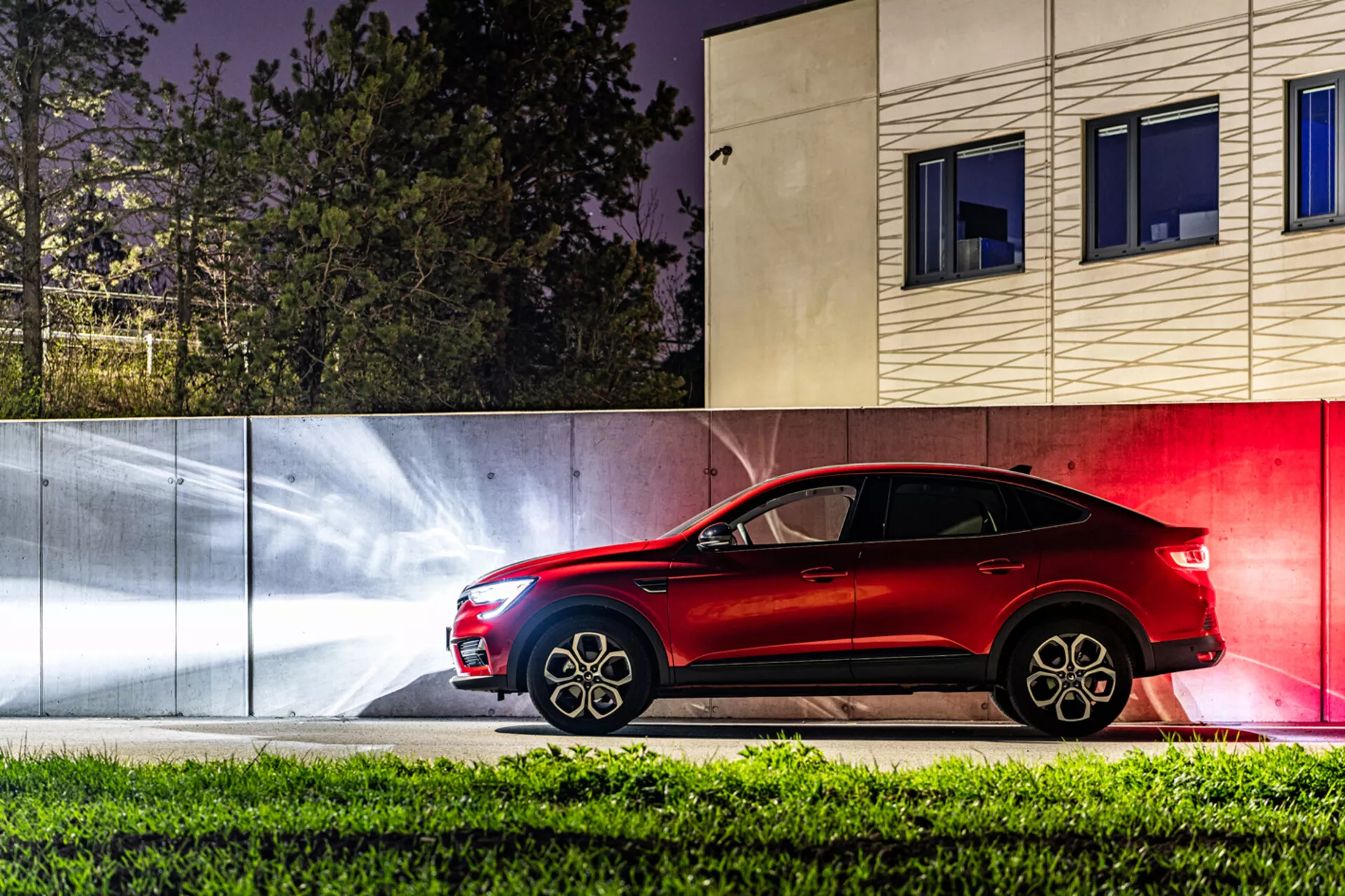 Vista lateral do Renault Arkana 2021 à noite com rastros de luz dinâmicos e contexto urbano contemporâneo, mostrando seu design elegante de SUV estilo cupê e tecnologia de iluminação avançada.