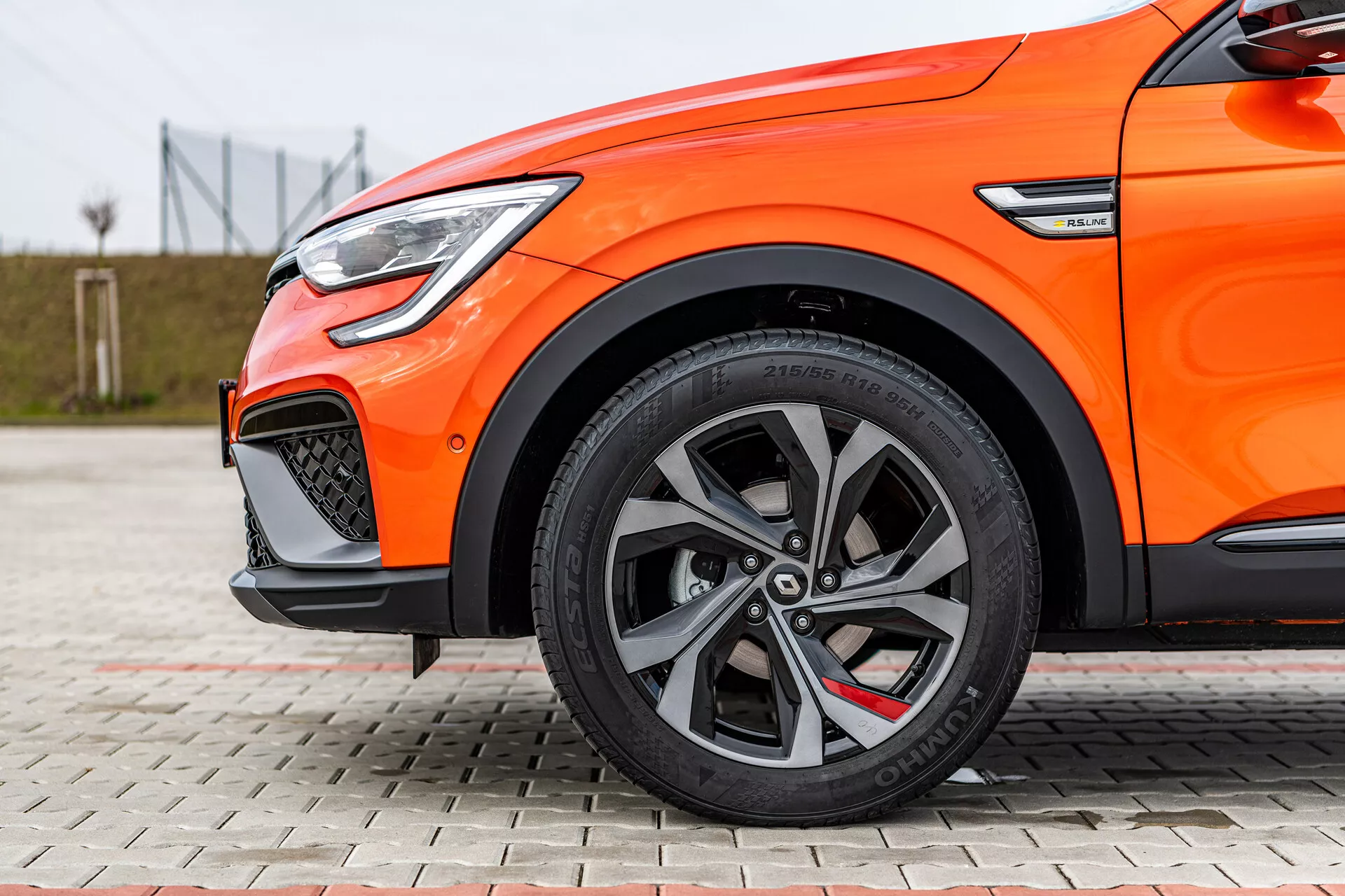 Vista lateral de perto de um Renault Arkana 2021 laranja destacando rodas de liga leve multiraiadas, pneus de perfil baixo, sistema de freio de alto desempenho e luz diurna em LED