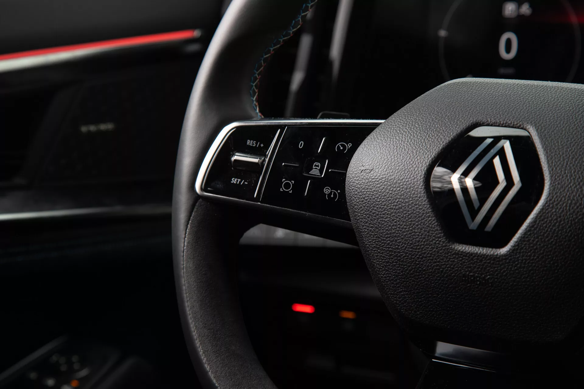 Vista interior do Renault Austral 2022 destacando os controles no volante e o emblema, incluindo funções de botão iluminado para volume, chamadas, comandos de voz e navegação no infotainment, da perspectiva do assento do motorista.